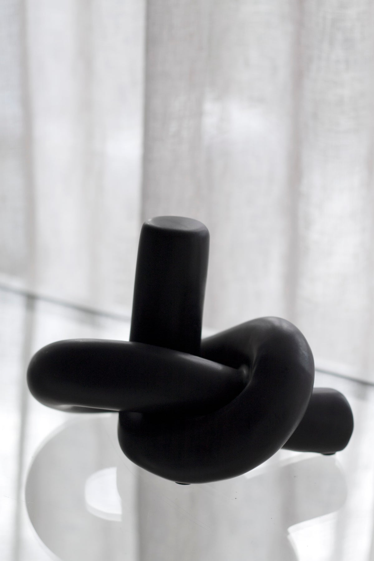 Black Knot Ornament on a round white table in soft light, sheer curtain behind