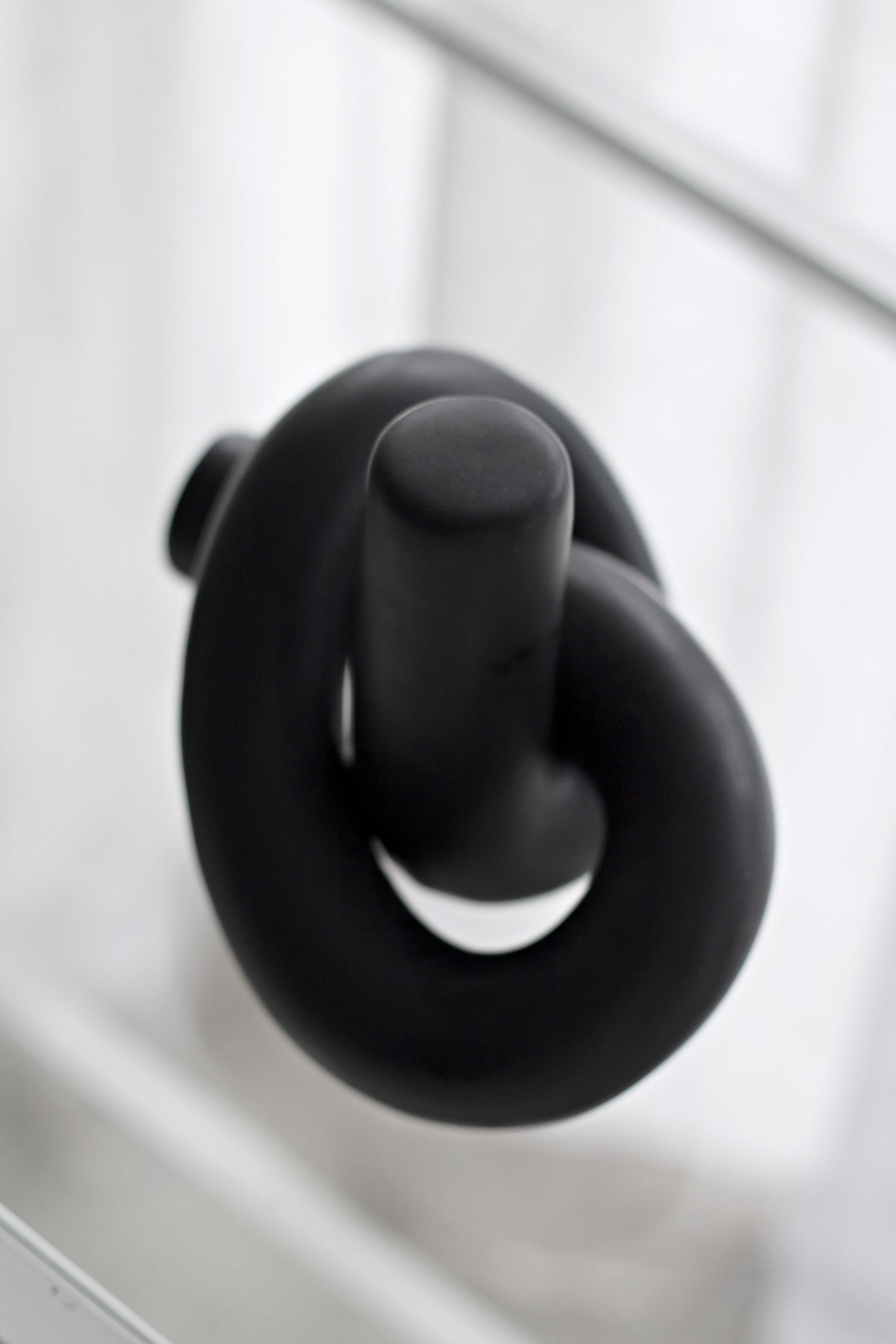 Black Knot Ornament from a low angle on a white ledge, sheer curtain behind