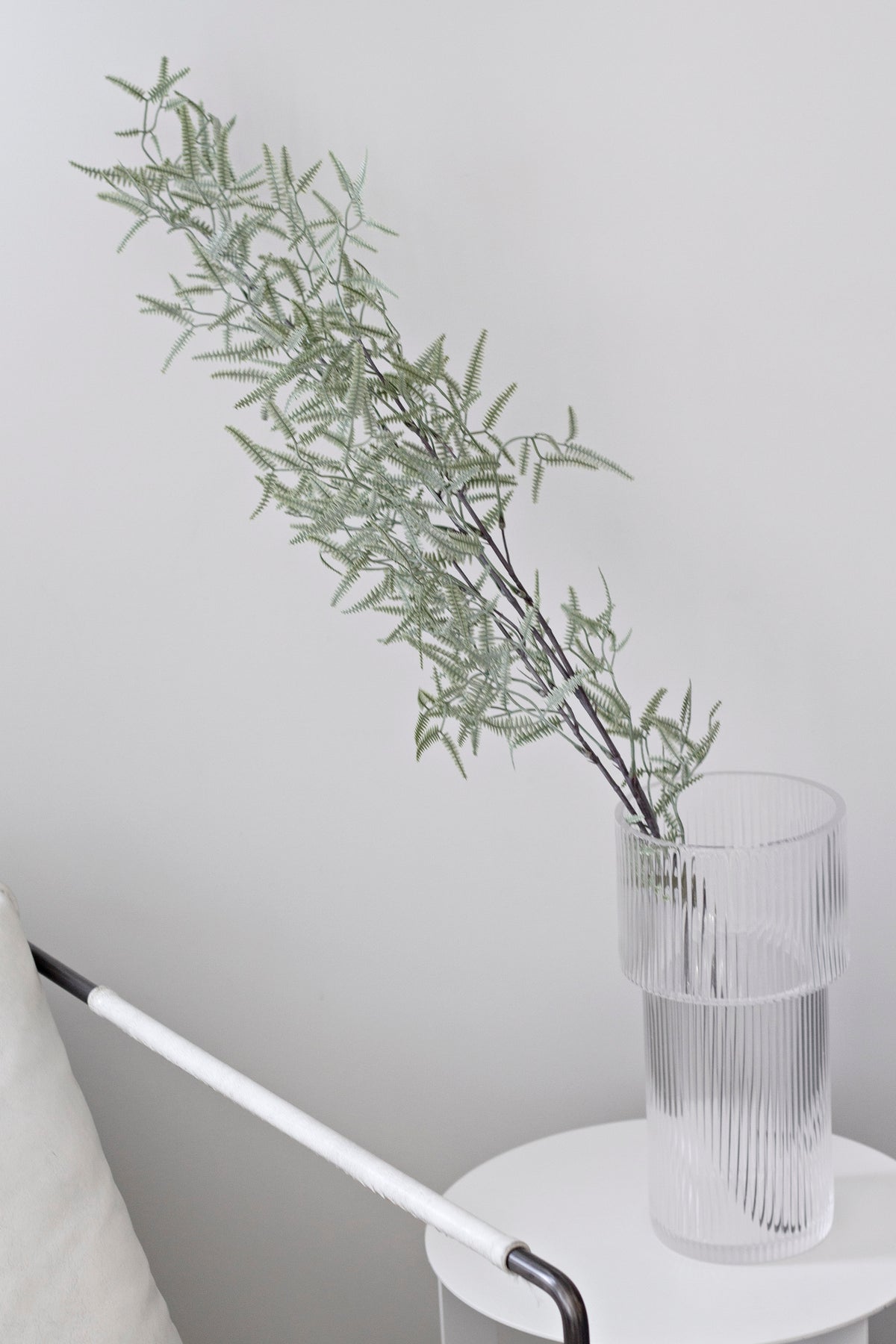 Faux kowhai stem in a ribbed glass vase on a white side table