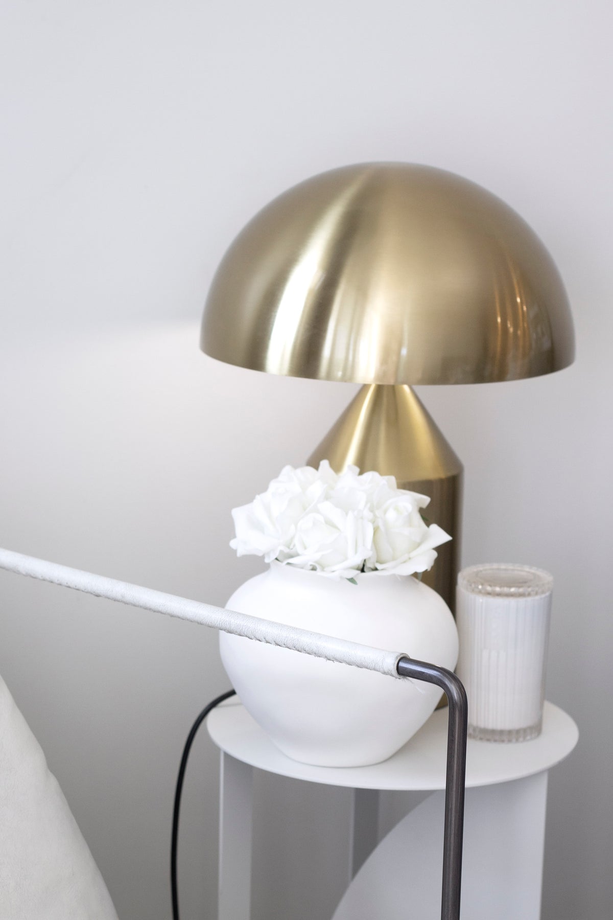 Brass dome lamp beside white roses in a round white vase on a small side table