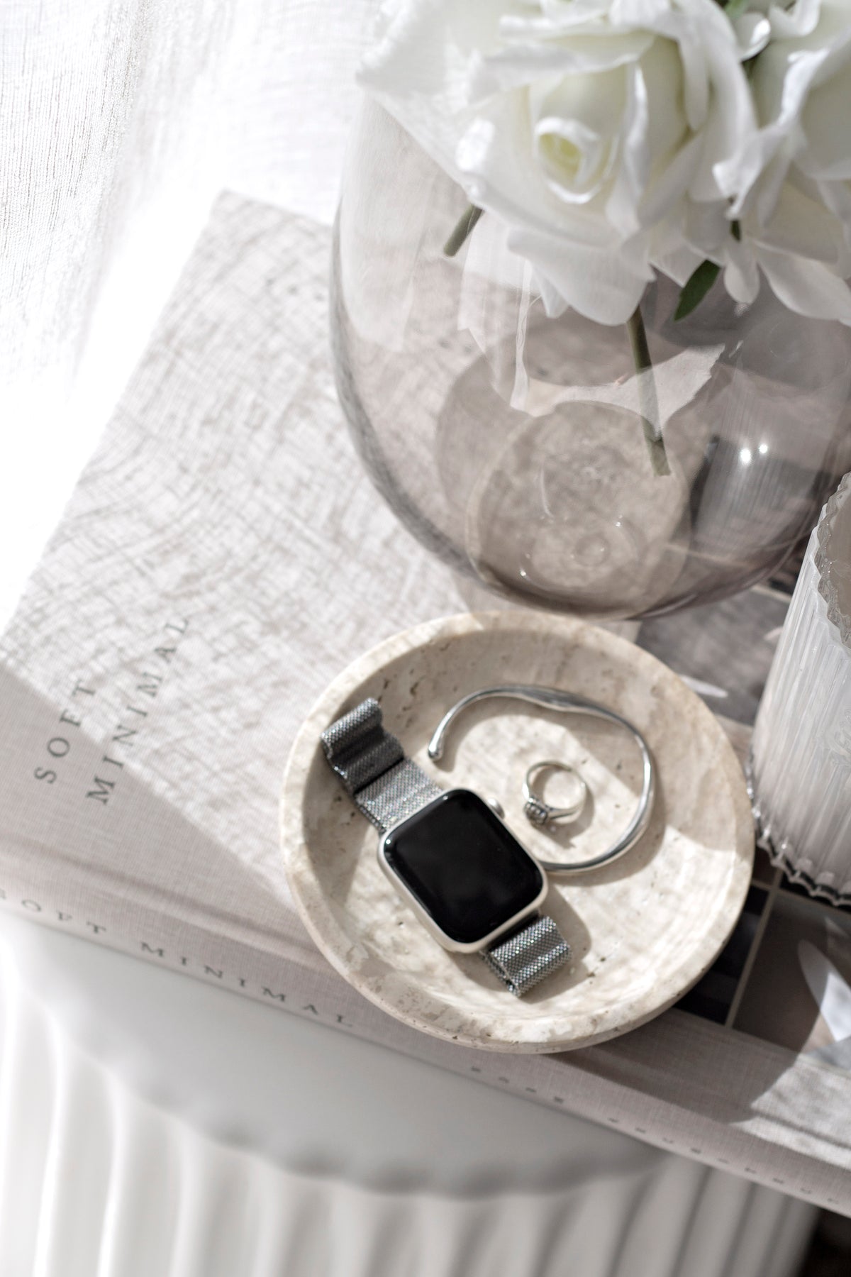Looking down on the tray holding a watch and rings, a glass vase of roses alongside