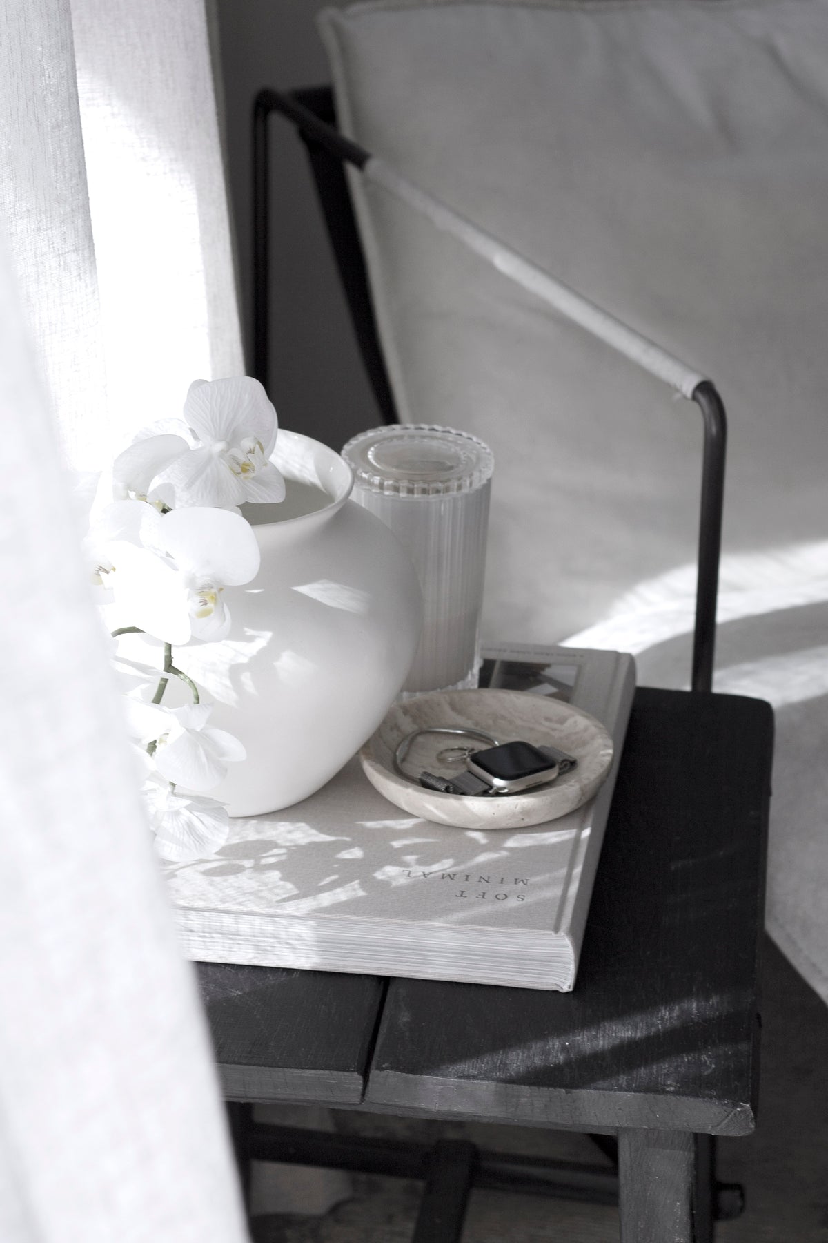 Travertine tray of jewellery beside a white vase of orchids and a ribbed candle