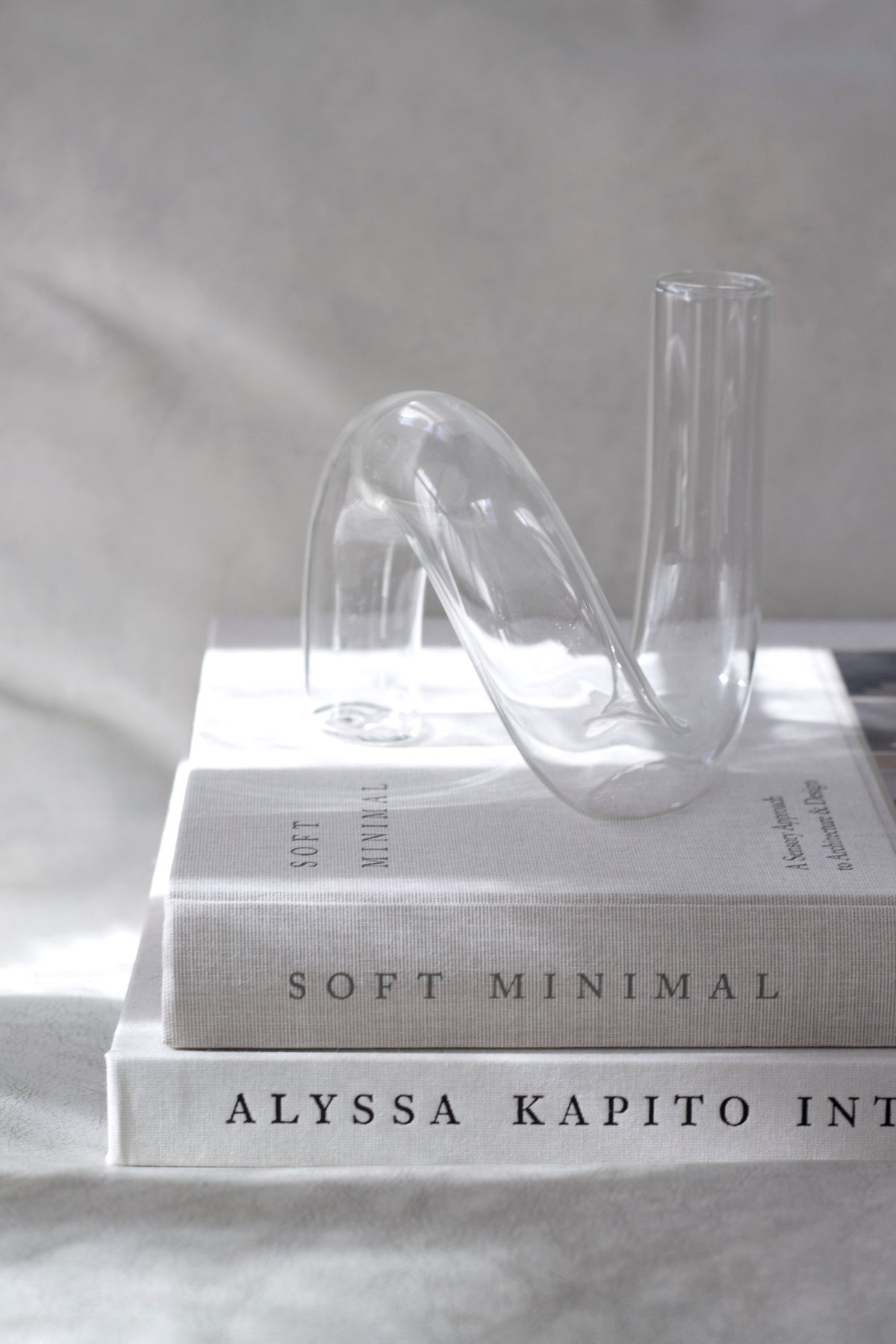 Two clear glass vases standing on a stack of three books on soft grey linen