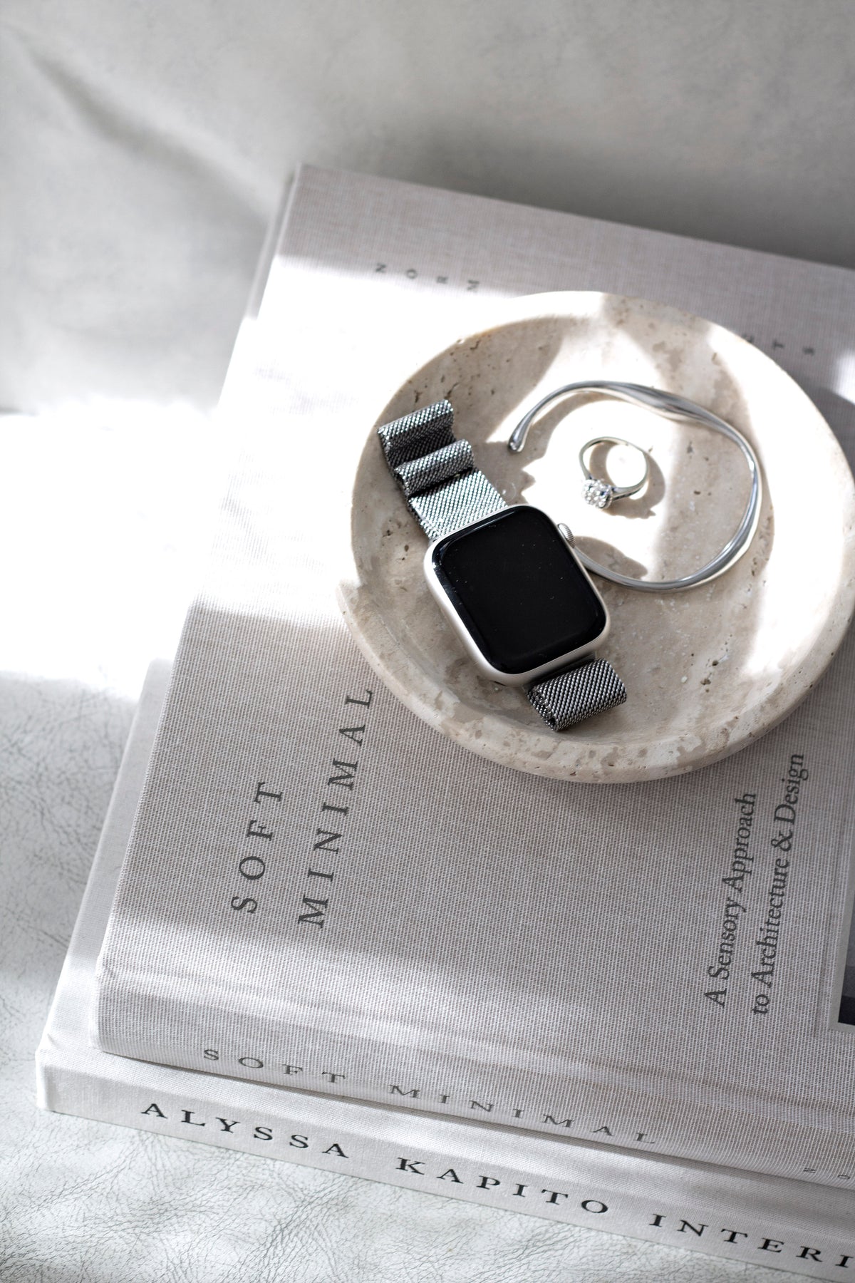 Watch and a ring in the travertine tray on a stack of interiors books