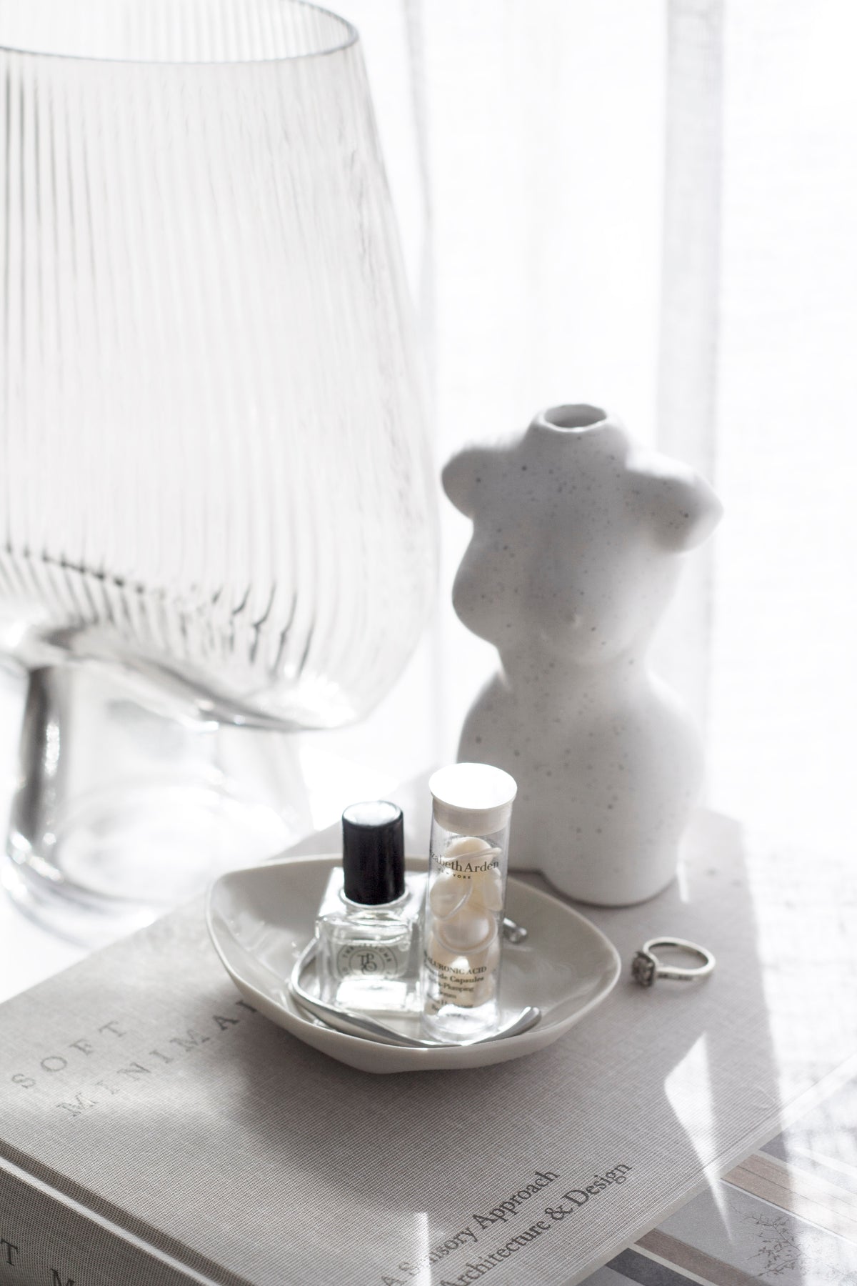 Close-up of a white ceramic mini torso vase styled on books with a ring dish, perfume bottle, and soft filtered light.