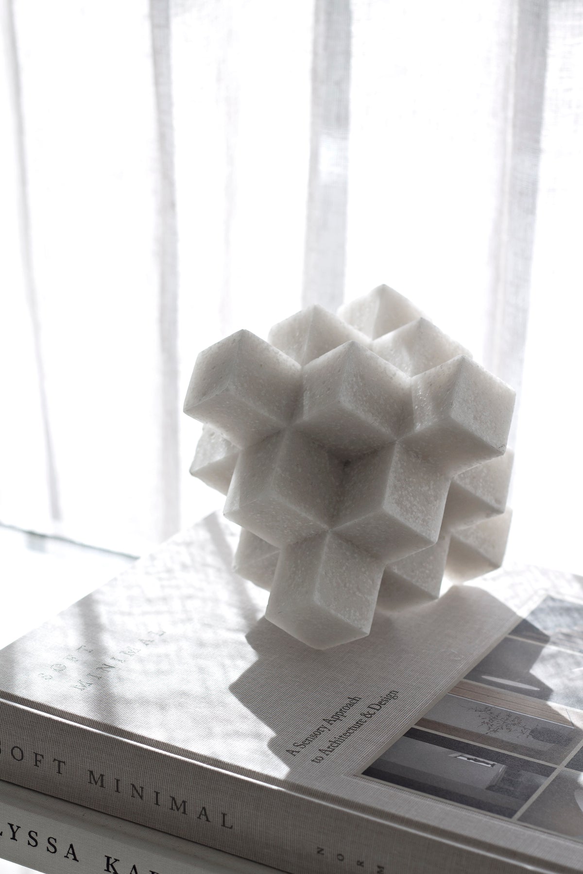 White Cubism sculpture on books by a window, cubes in strong shadow