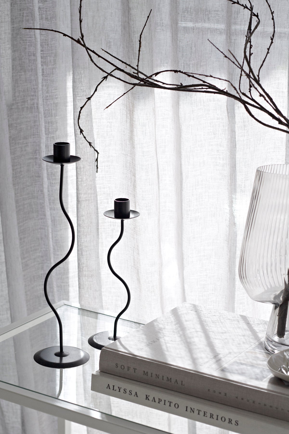 Black Hera pair standing on books with a ribbed glass vase behind and light through linen