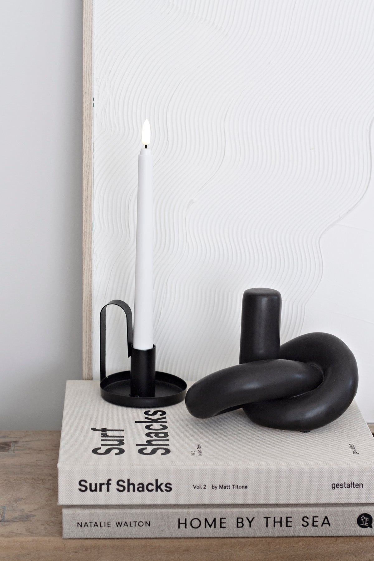 Black Knot Ornament beside a black candlestick with a lit ivory taper, on stacked books
