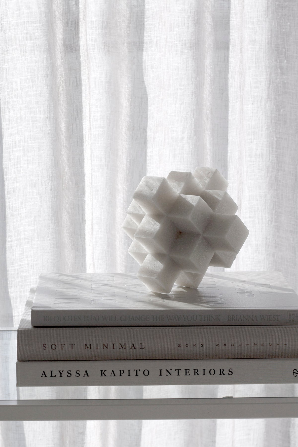 White Cubism sculpture on a stack of books beside a sheer curtain