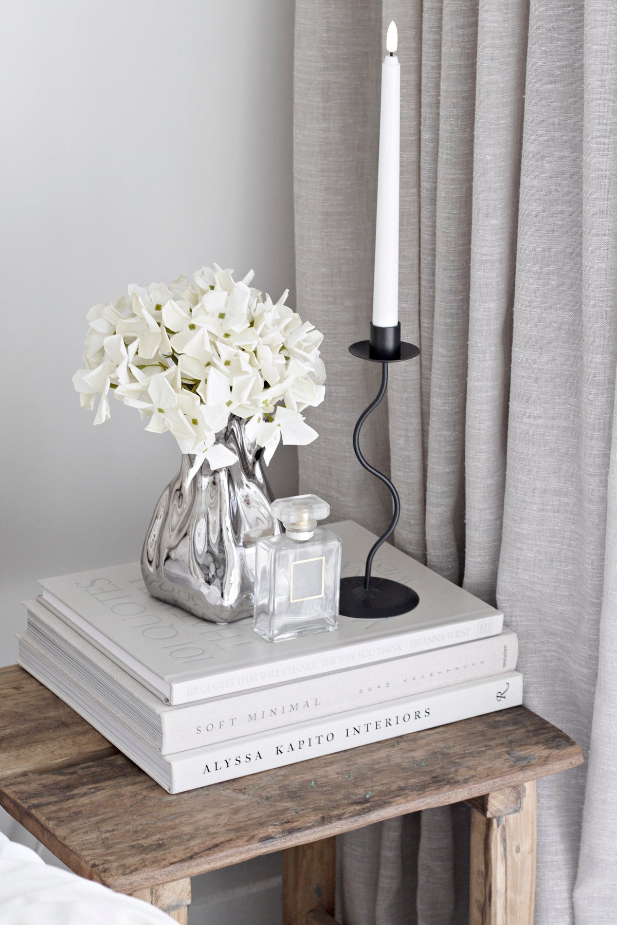 Black Hera holder with a white taper beside white blooms on books on a timber stool