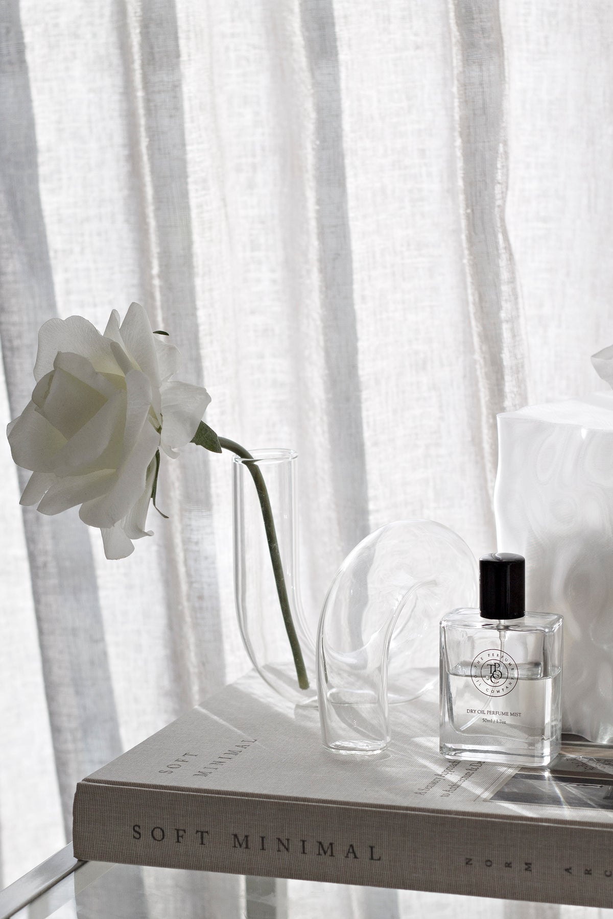 Wider view of the clear J-Curve vase with a white rose draping over the book stack