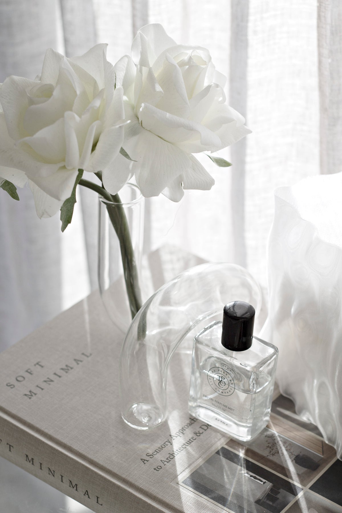 Clear J-Curve vase holding white roses on a shelf beside a small fragrance bottle