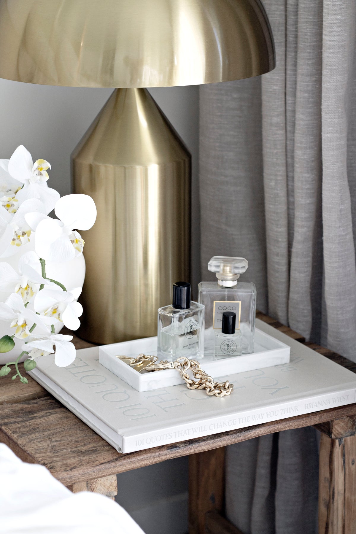 Brass dome lamp on a rustic bedside with perfume bottles on a marble tray and a gold chain