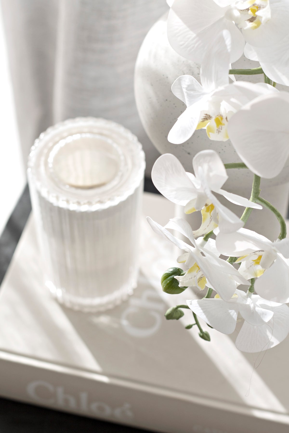 White moth orchid in a ribbed white vessel on a tray, blooms arching over the rim