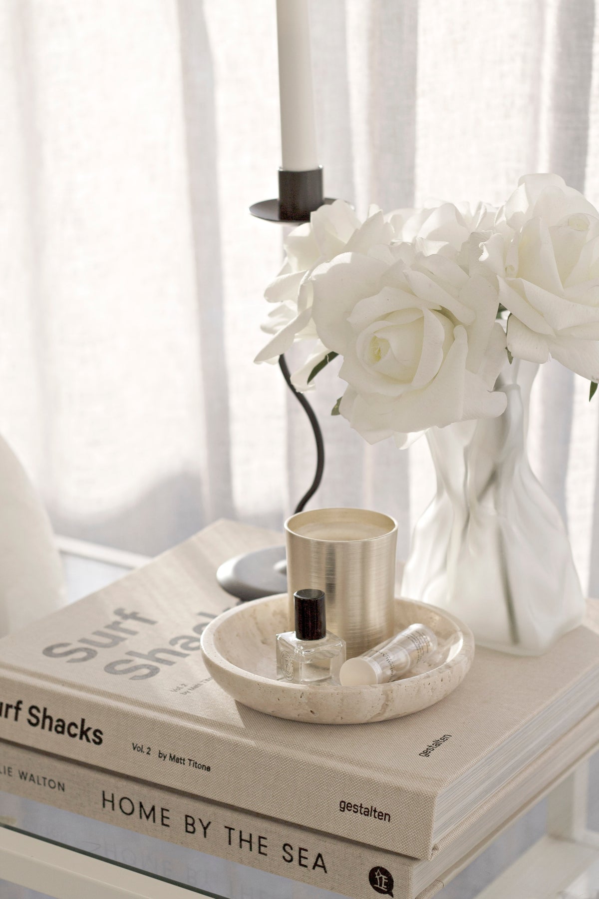 Candle in the travertine tray on a stack of books, white roses and a taper behind