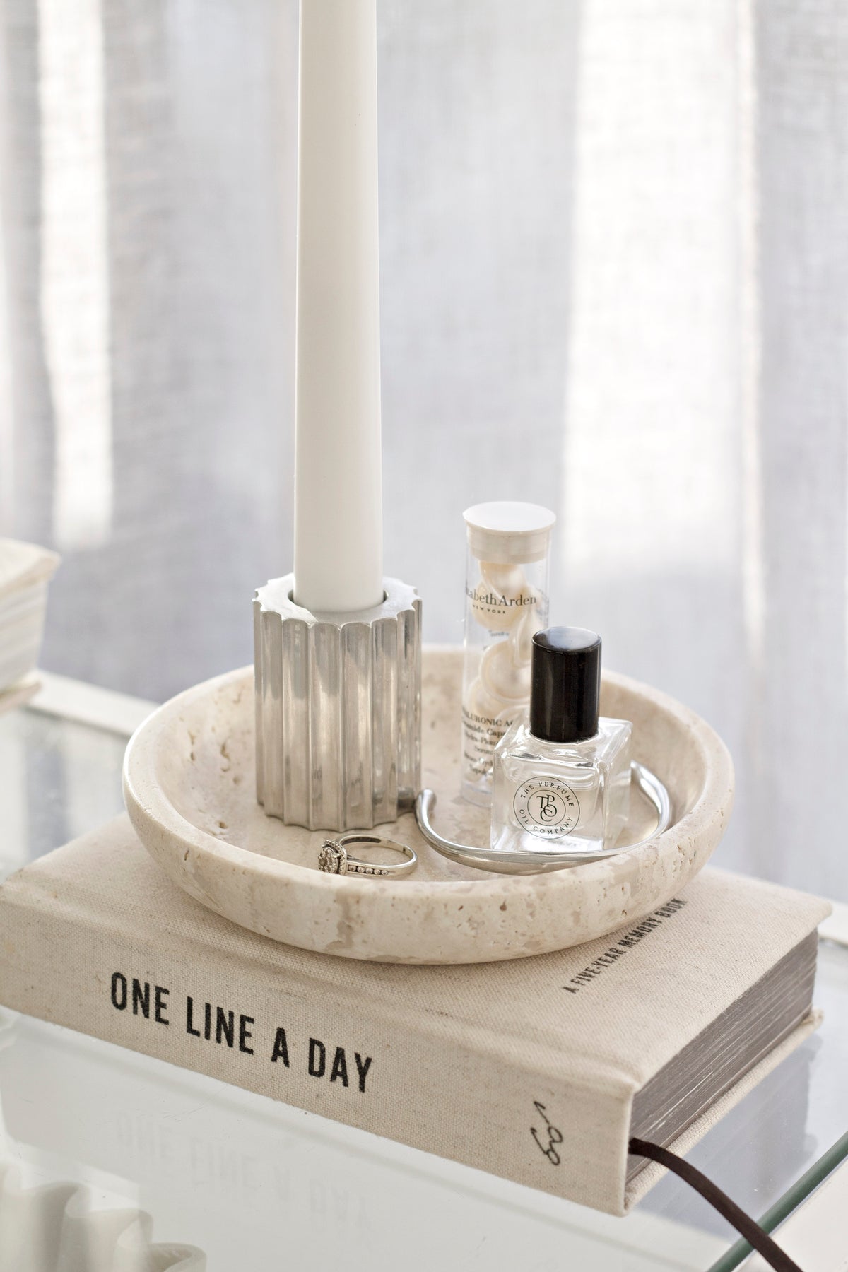 Perfume bottle and a fluted candlestick standing in the travertine tray on a book