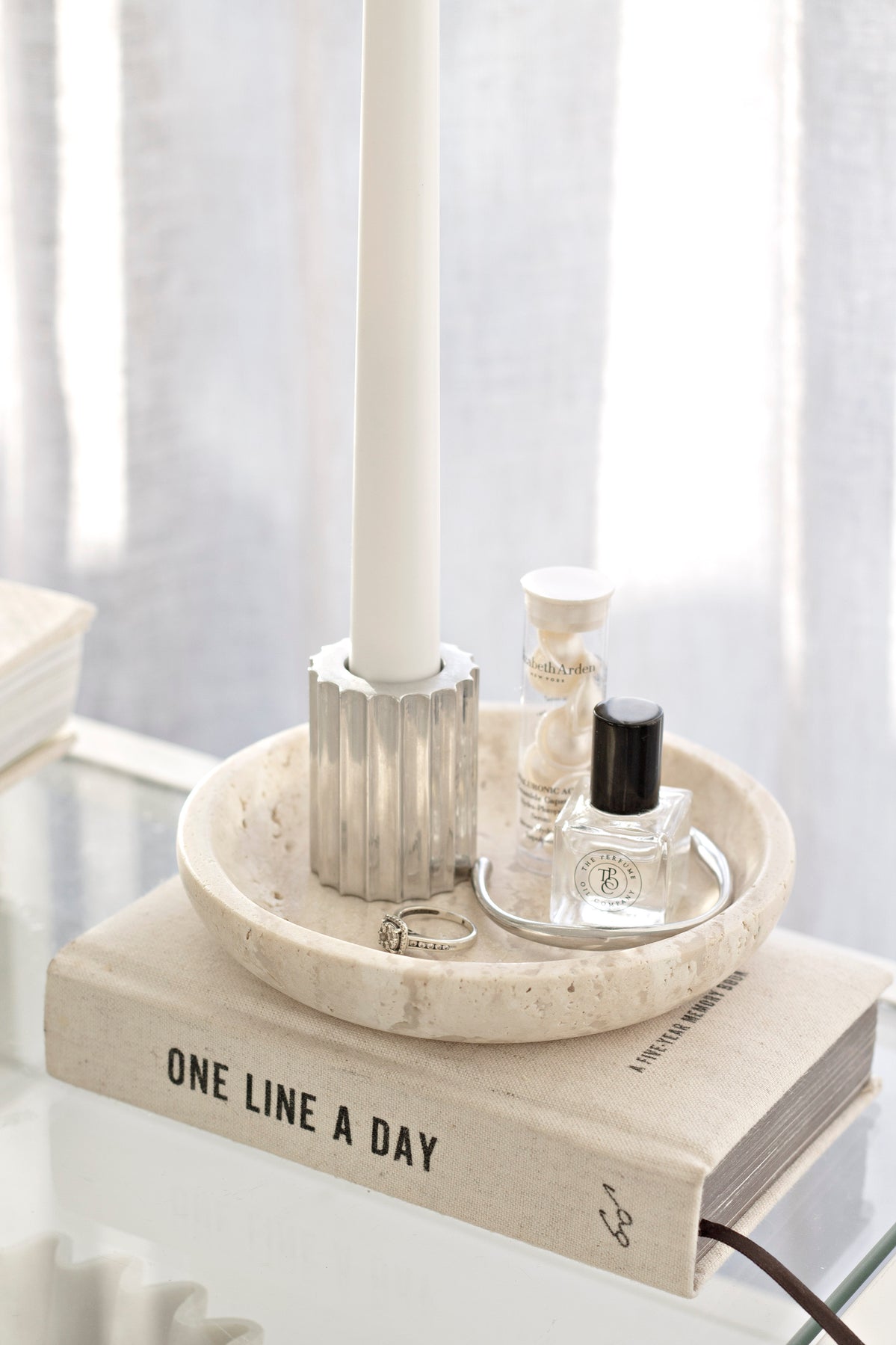 One Line a Day journal on a marble tray with a taper candle and perfume bottles beside a window