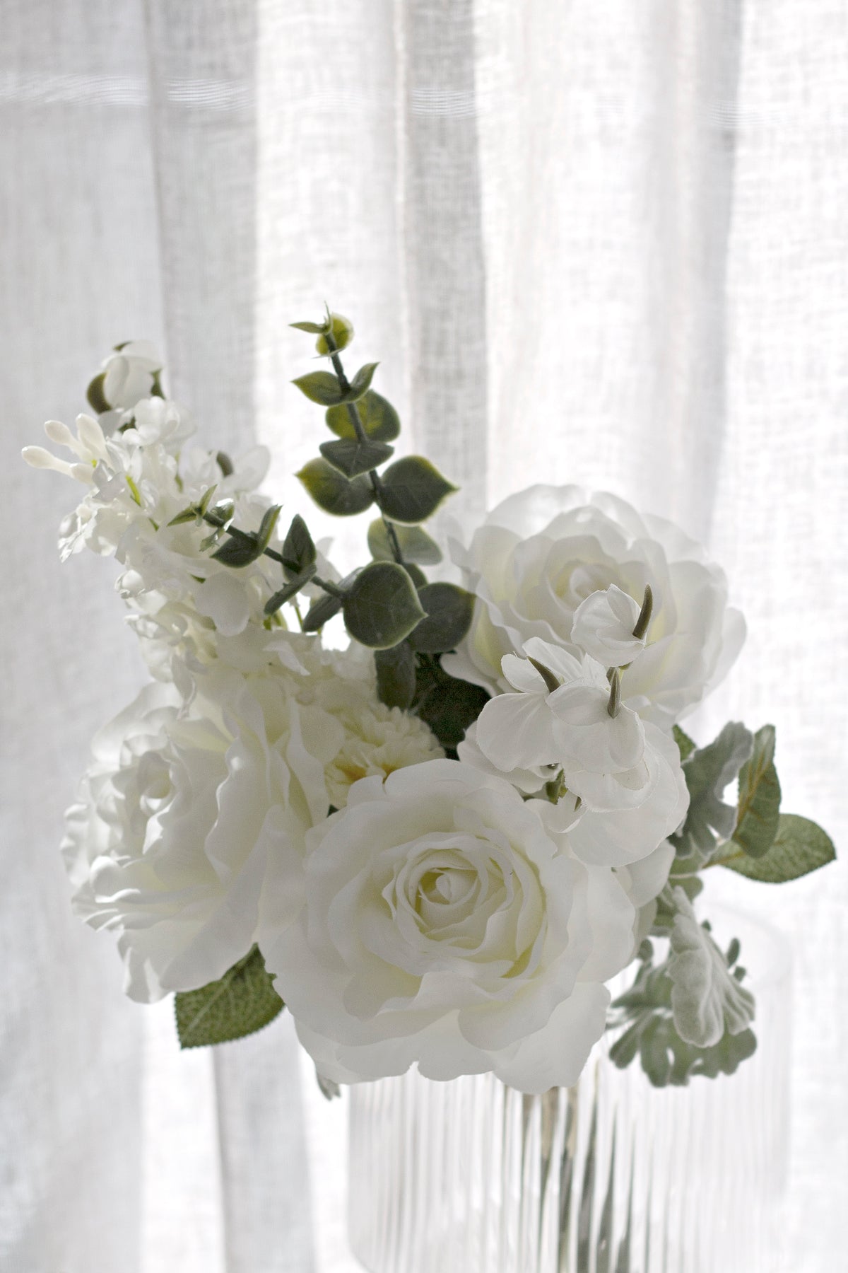 White faux bouquet in a ribbed glass vase by sheer curtains