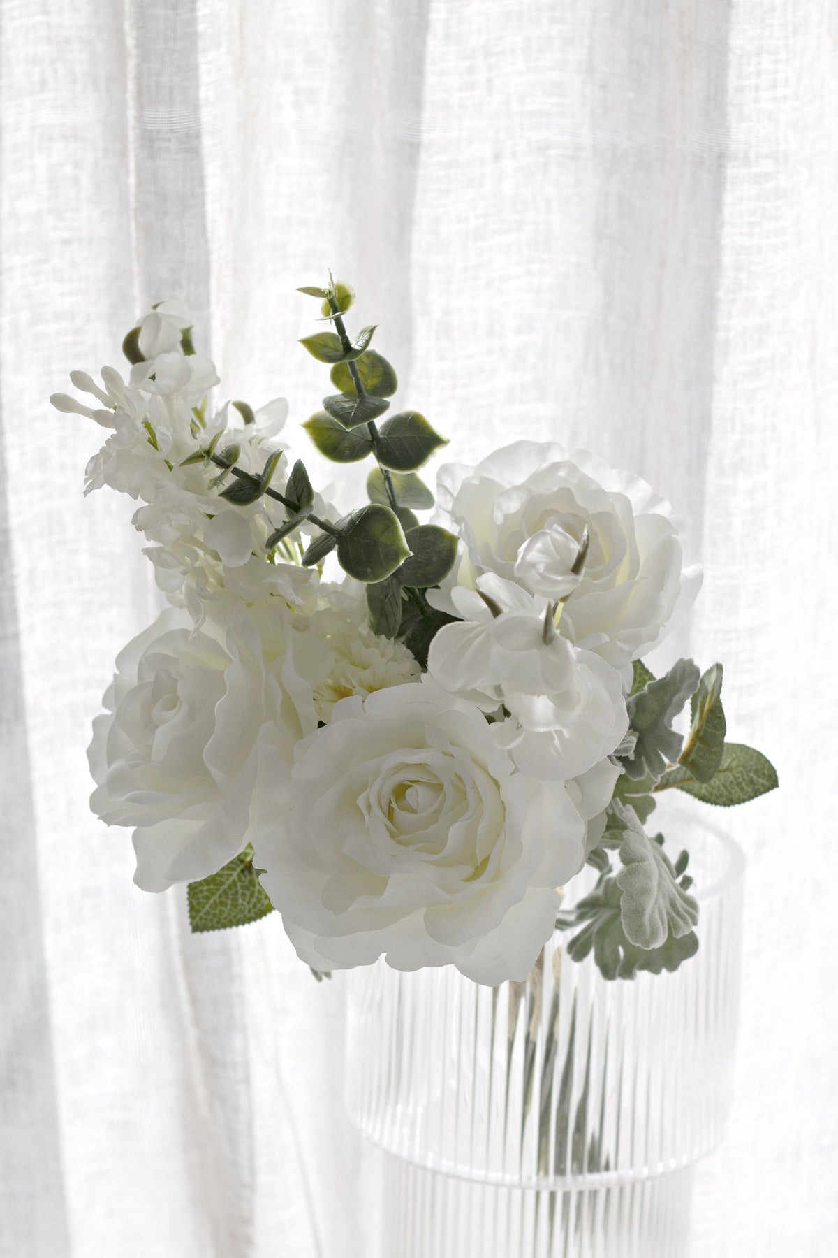 White faux bouquet with trailing eucalyptus by a curtain