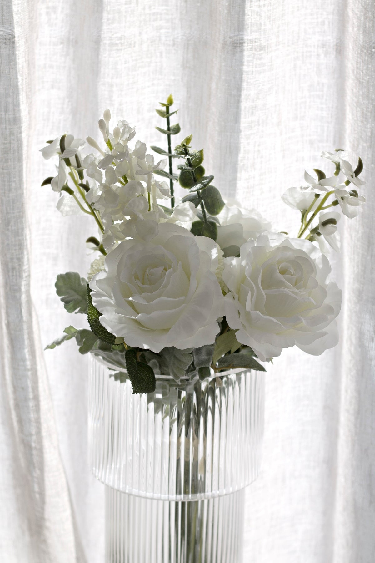 Tall view of the white faux bouquet in a ribbed glass vase