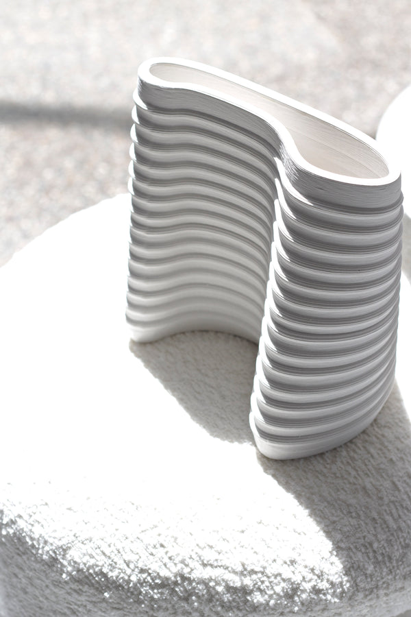 Fulk sculptural white ceramic vase with curved architectural lines, styled in bright sunlight on a soft boucle surface in a minimalist interior setting.
