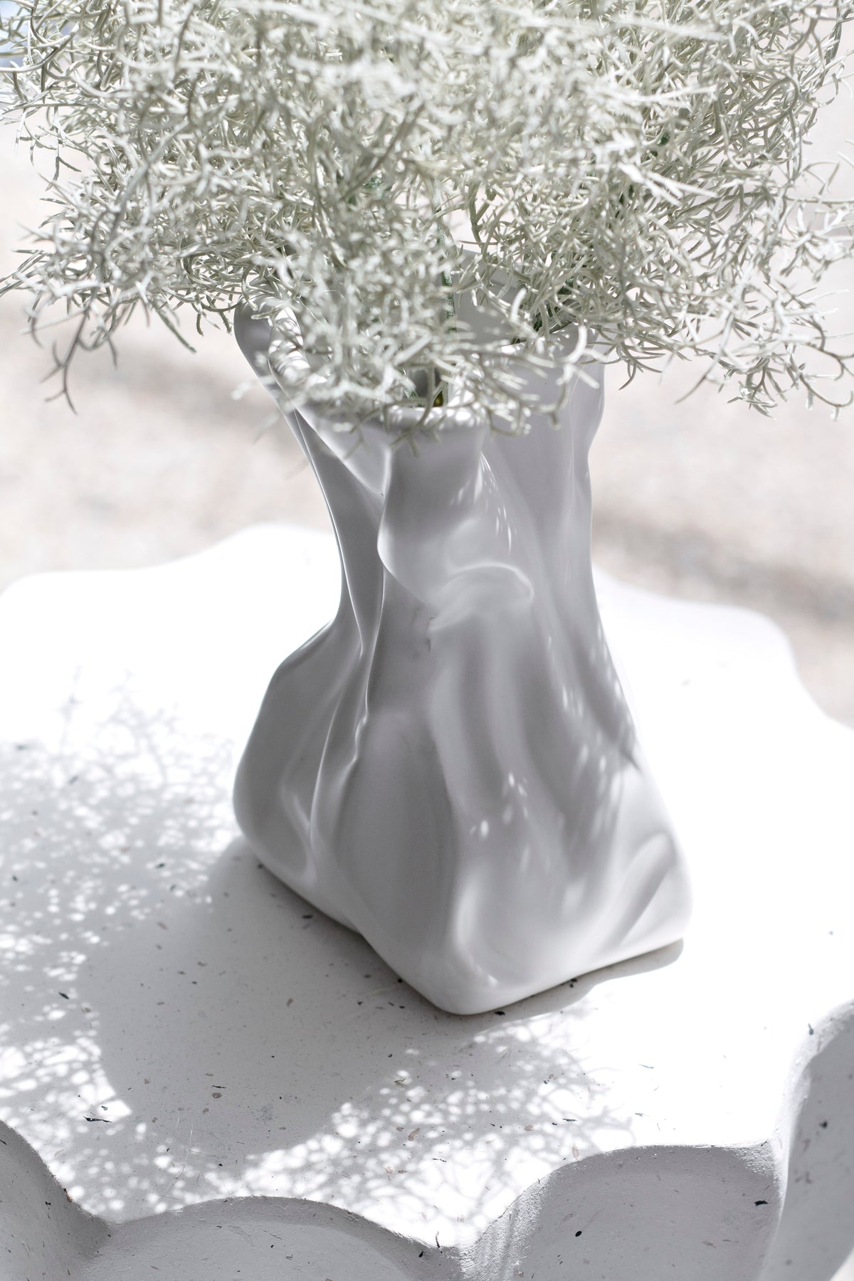 Cream crinkle vase of dried gypsophila standing on a scalloped stone tray