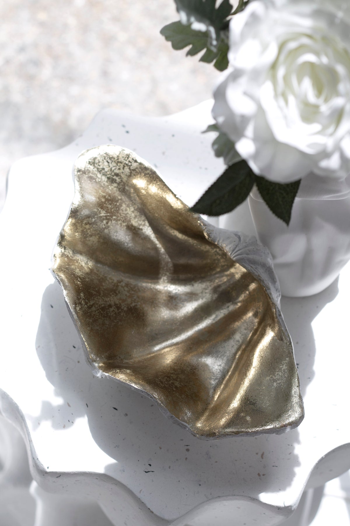 Clam shell bowl propped upright on a white surface with white roses behind