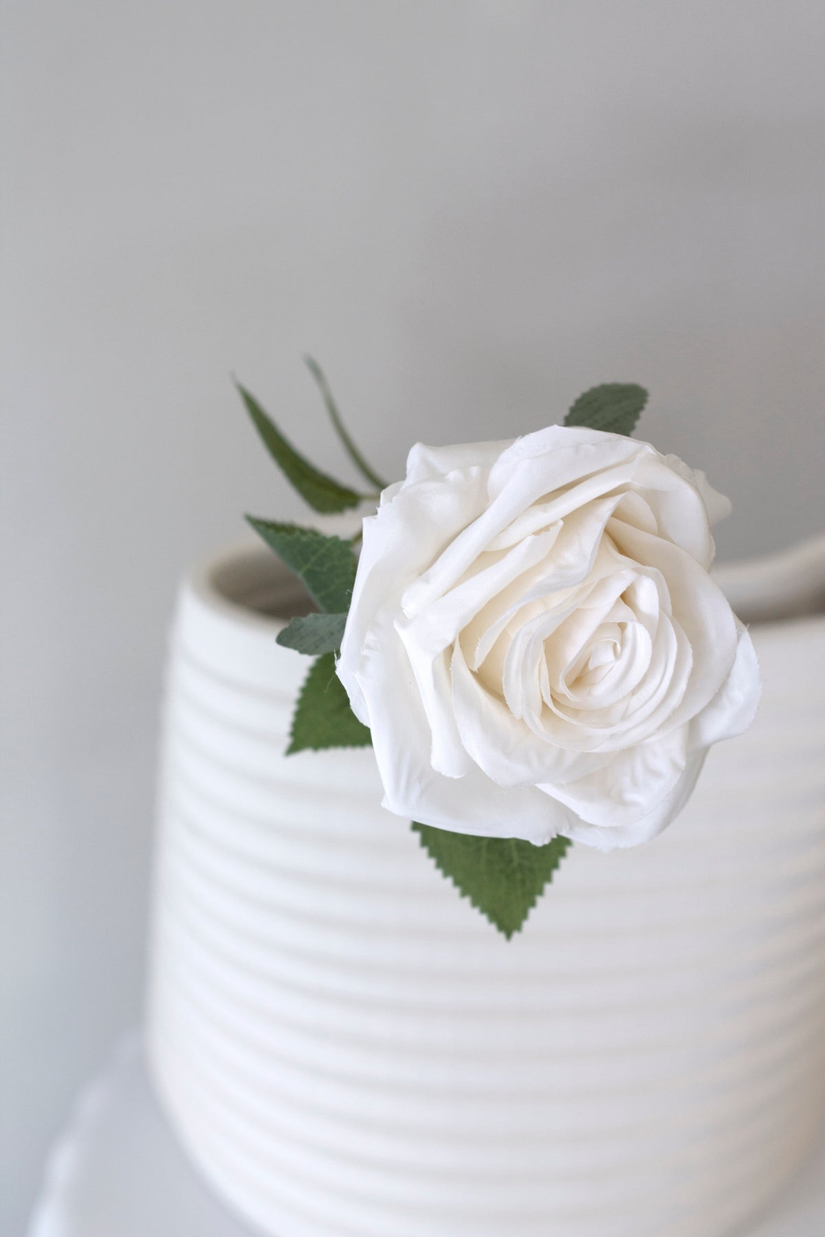 White faux rose resting over the rim of a ribbed white vase
