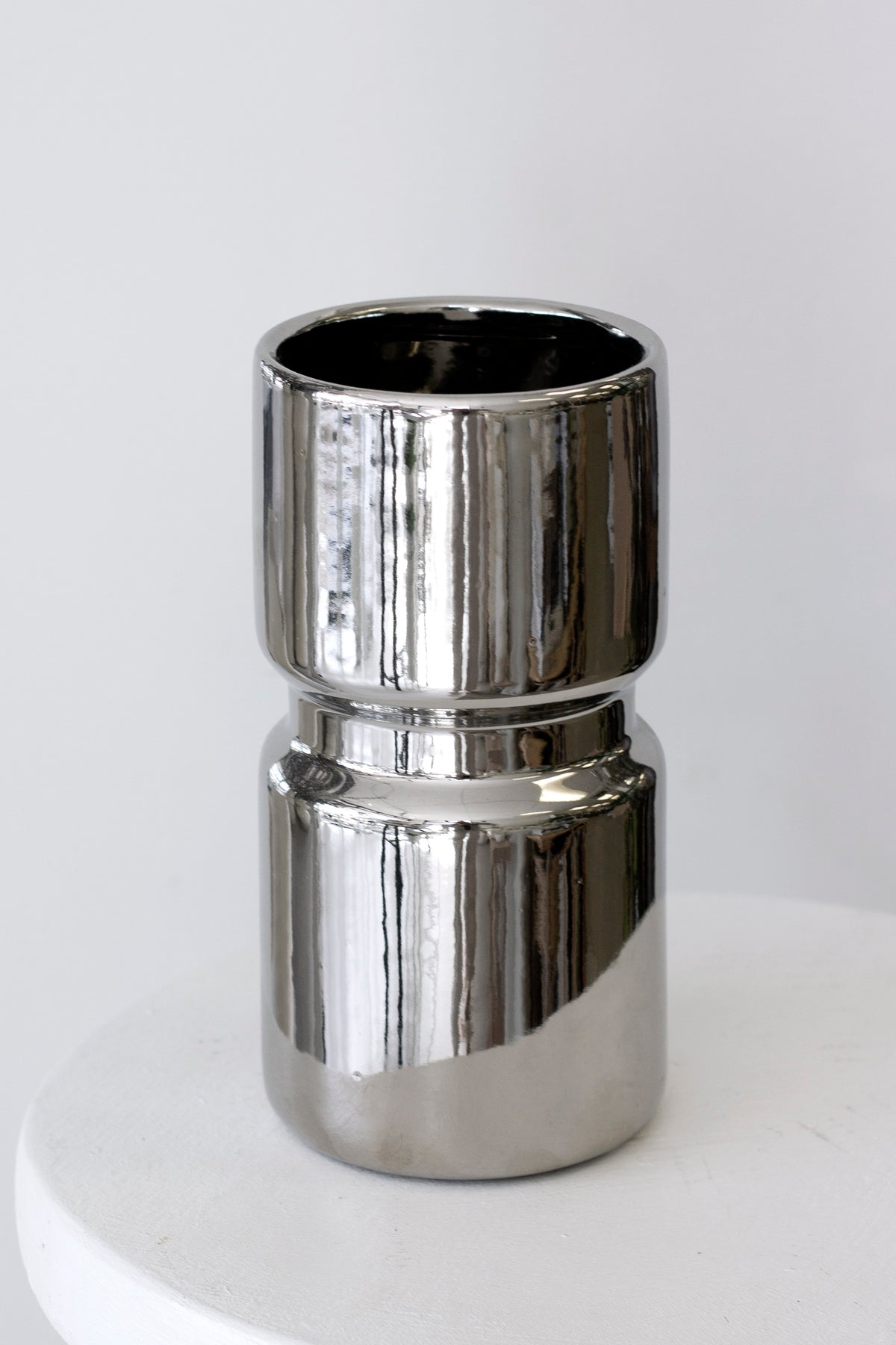 Silver cylinder vase on a pale surface, the mirrored finish catching the room