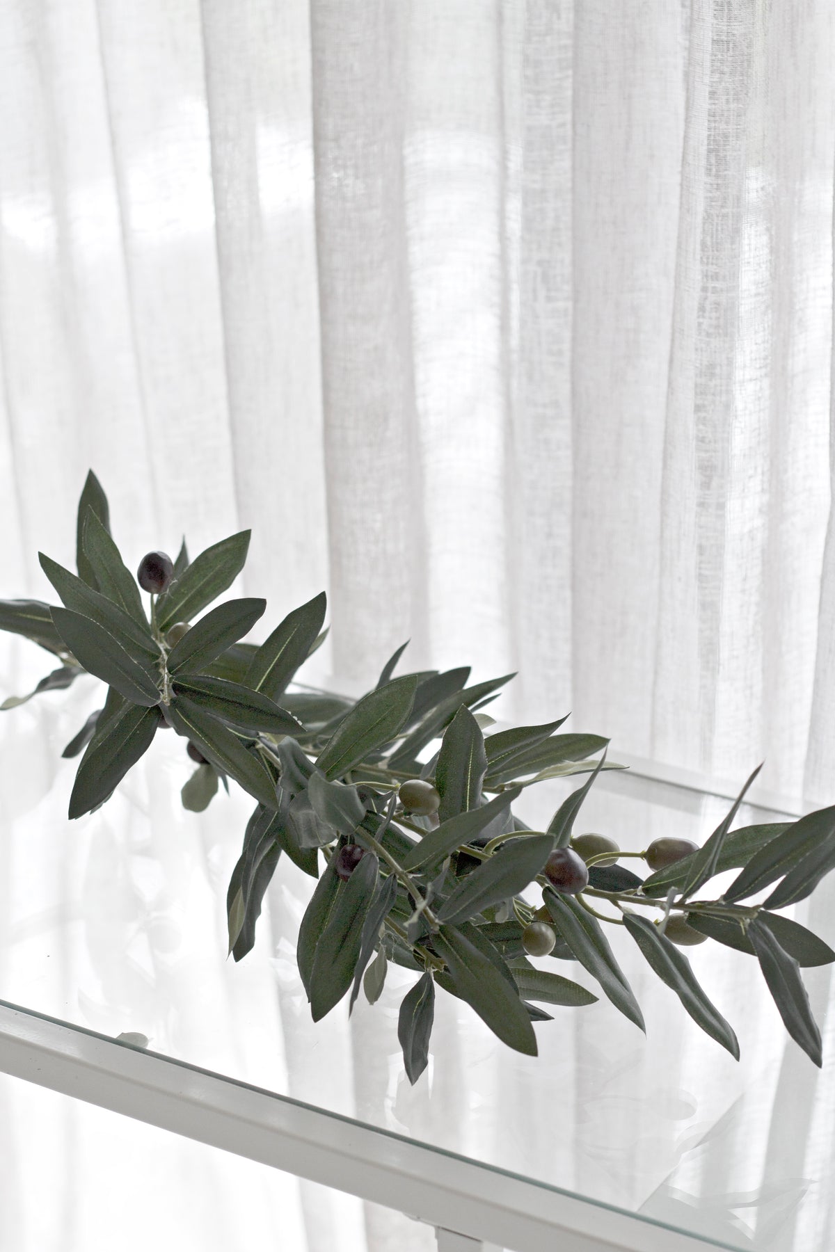 Olive branch resting across a white rail with a sheer curtain behind