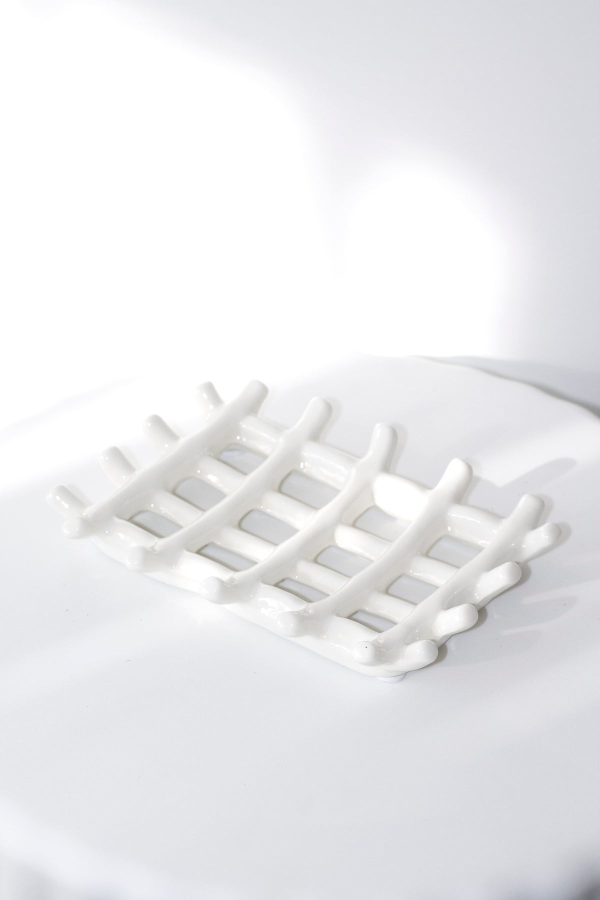 Soap dish on a curved white surface, soft shadow falling through the lattice