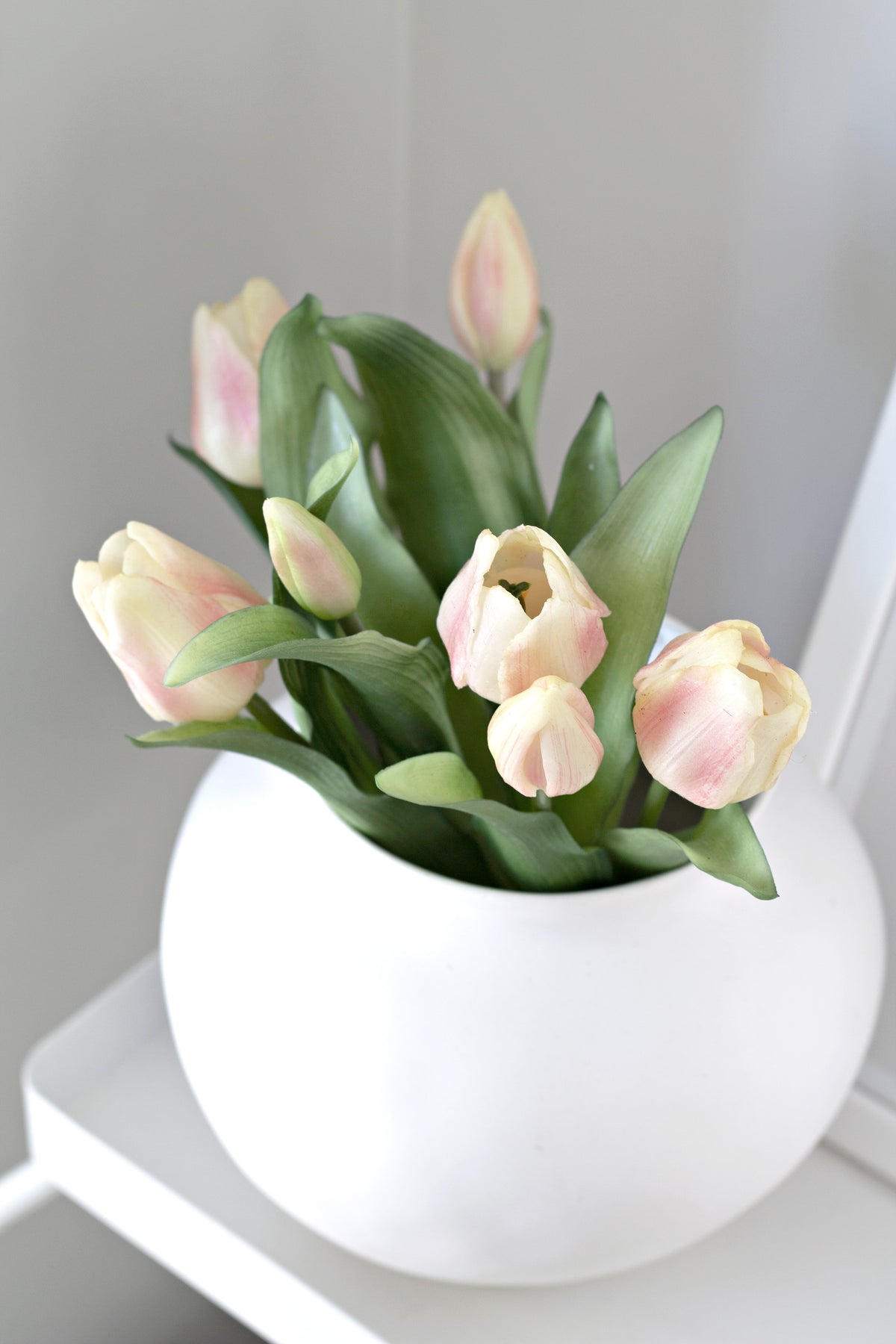 Pink and cream faux tulips in a round white ceramic vase on a white shelf