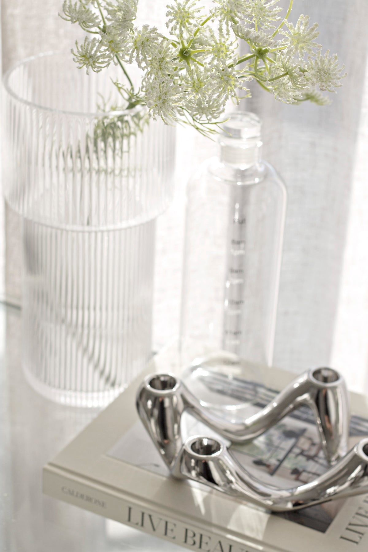 Silver candle holder on a book with a glass vase of fine white flowers alongside