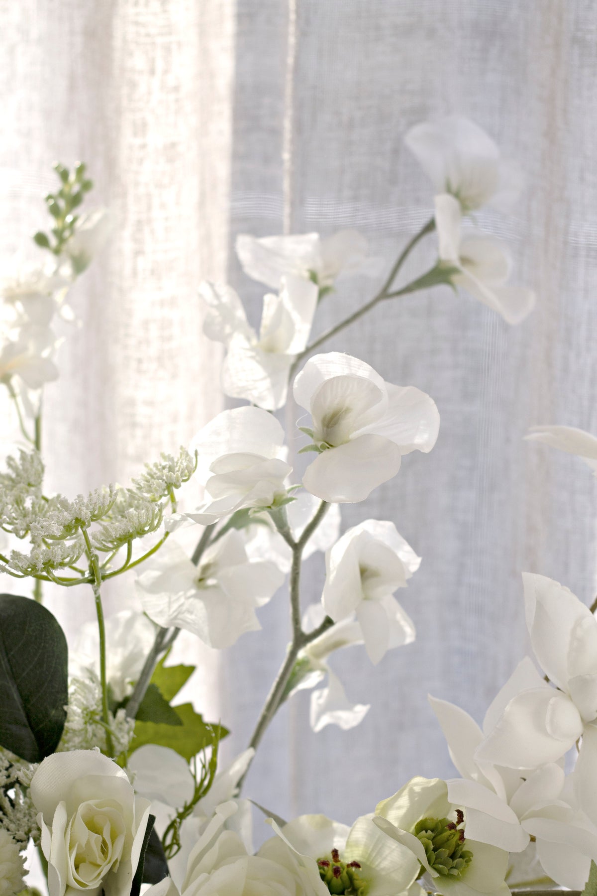 Sweet peas mixed with white flowers and greenery by a window