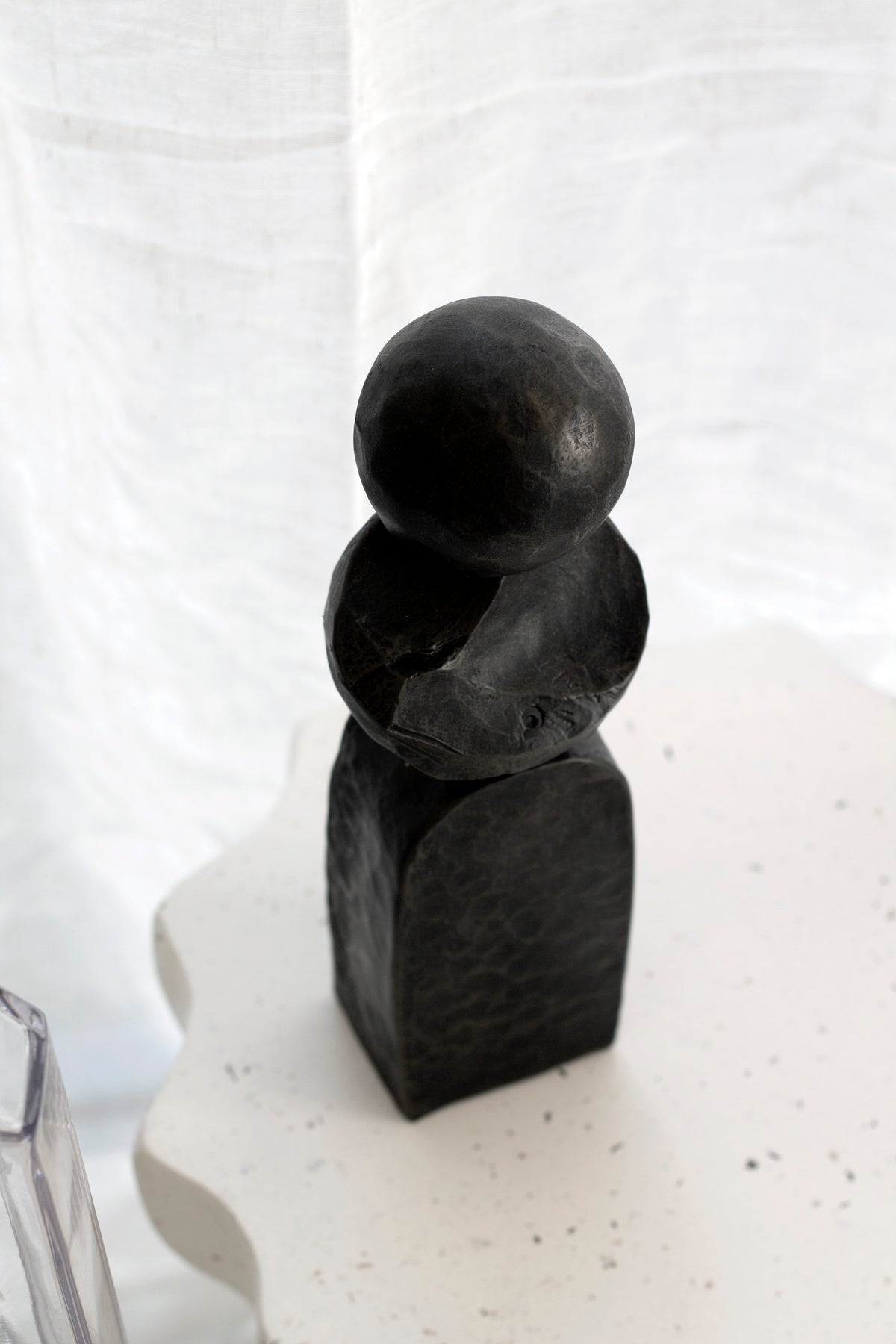 Small black Pillar sculpture on a pale speckled plinth, seen at an angle