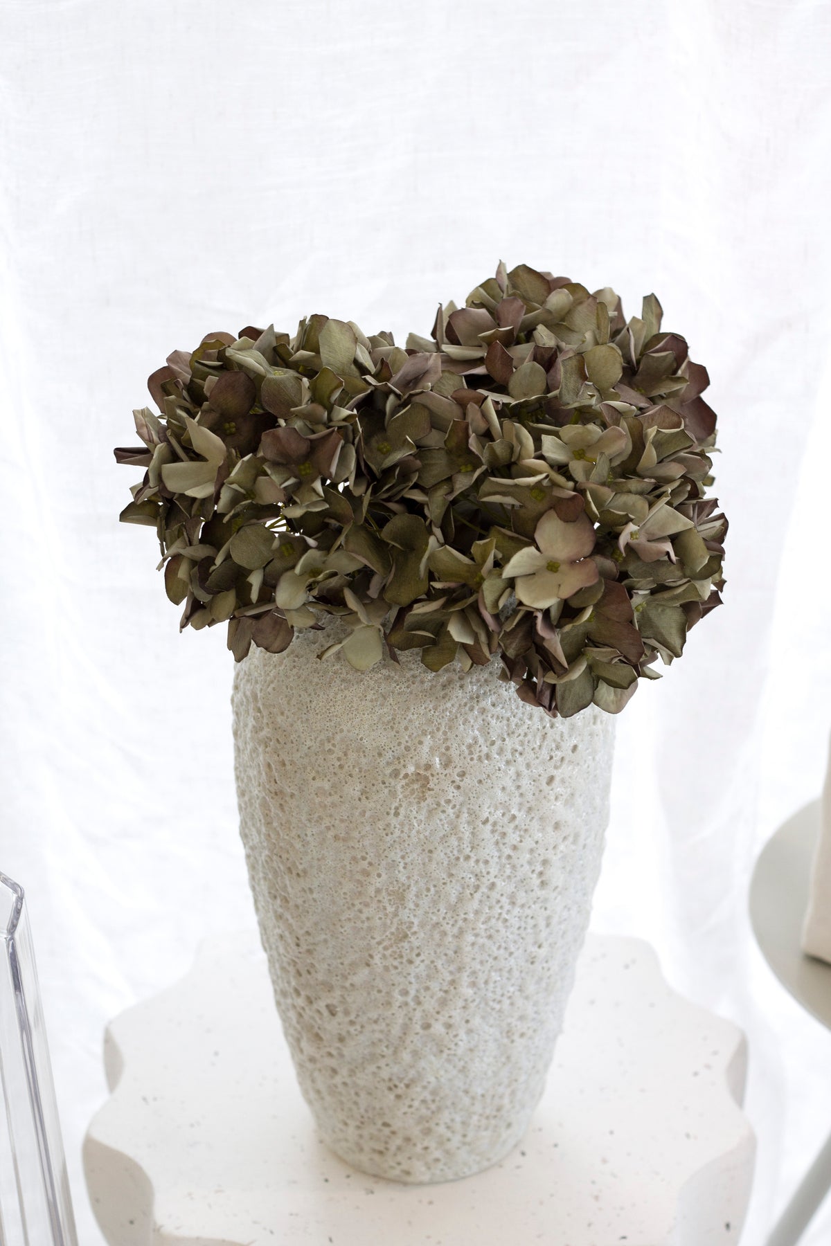 Green faux hydrangeas in a tall textured stone vase