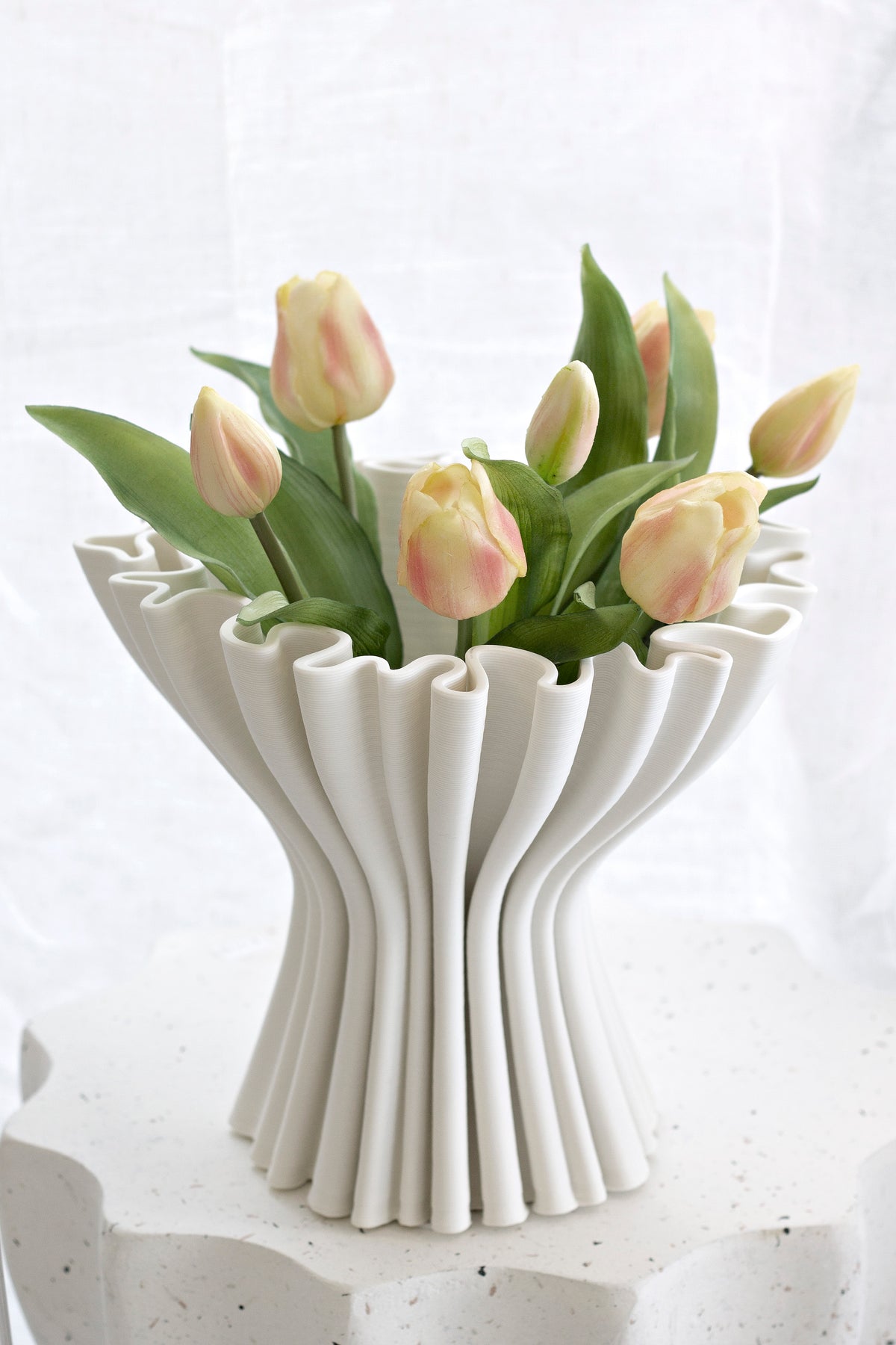 Peach and cream faux tulips in a fluted white ceramic vase on a textured plinth