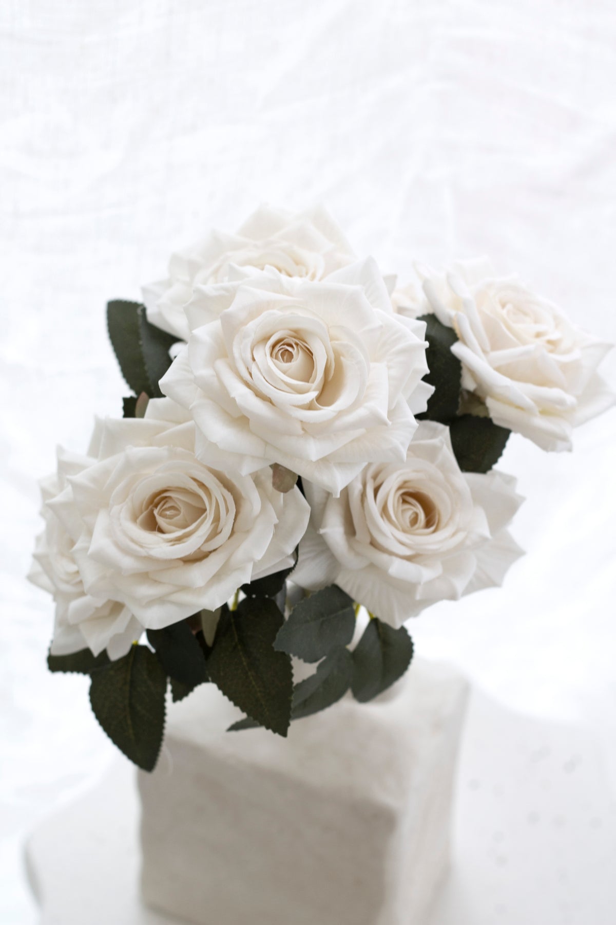 White roses with dark green leaves in a white stone look vase, close view