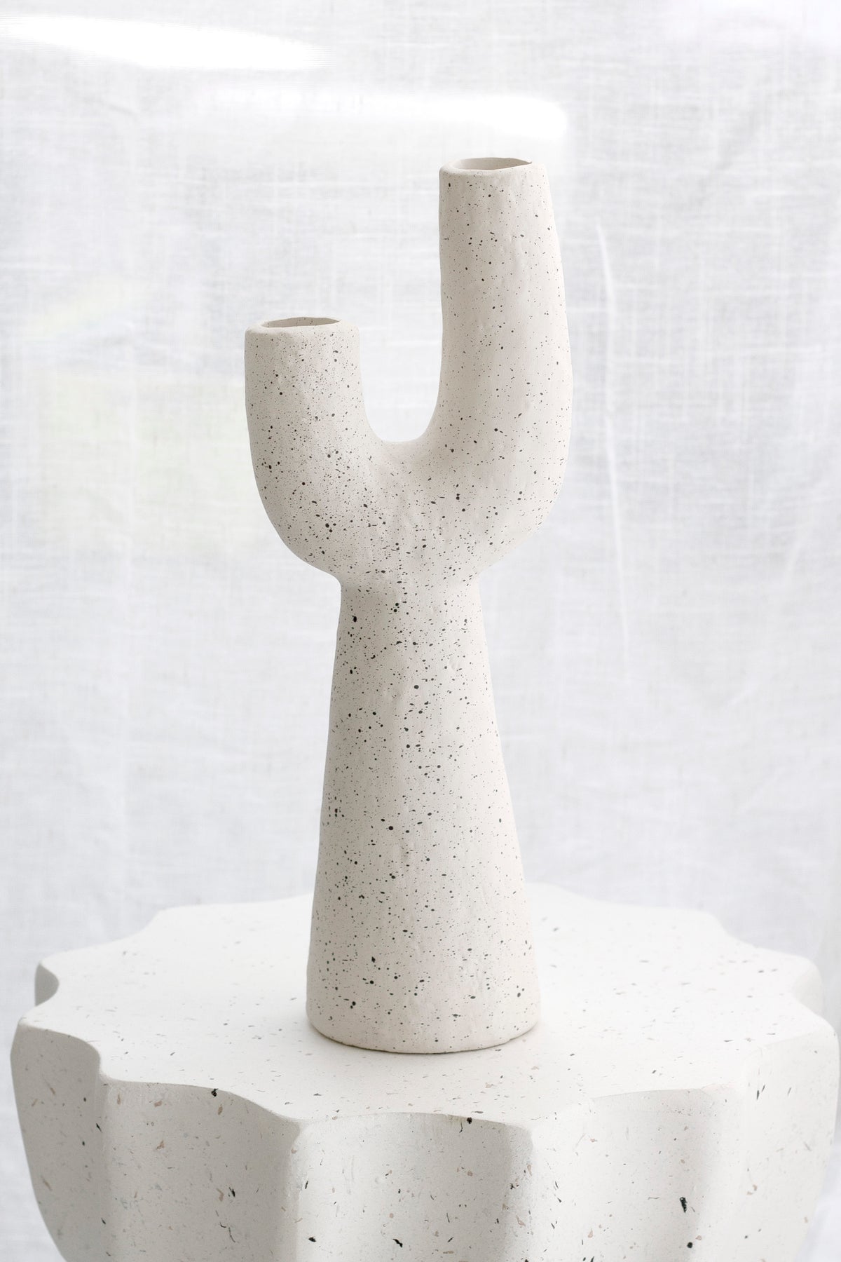 Franki cement vase on a white fluted pedestal in soft light