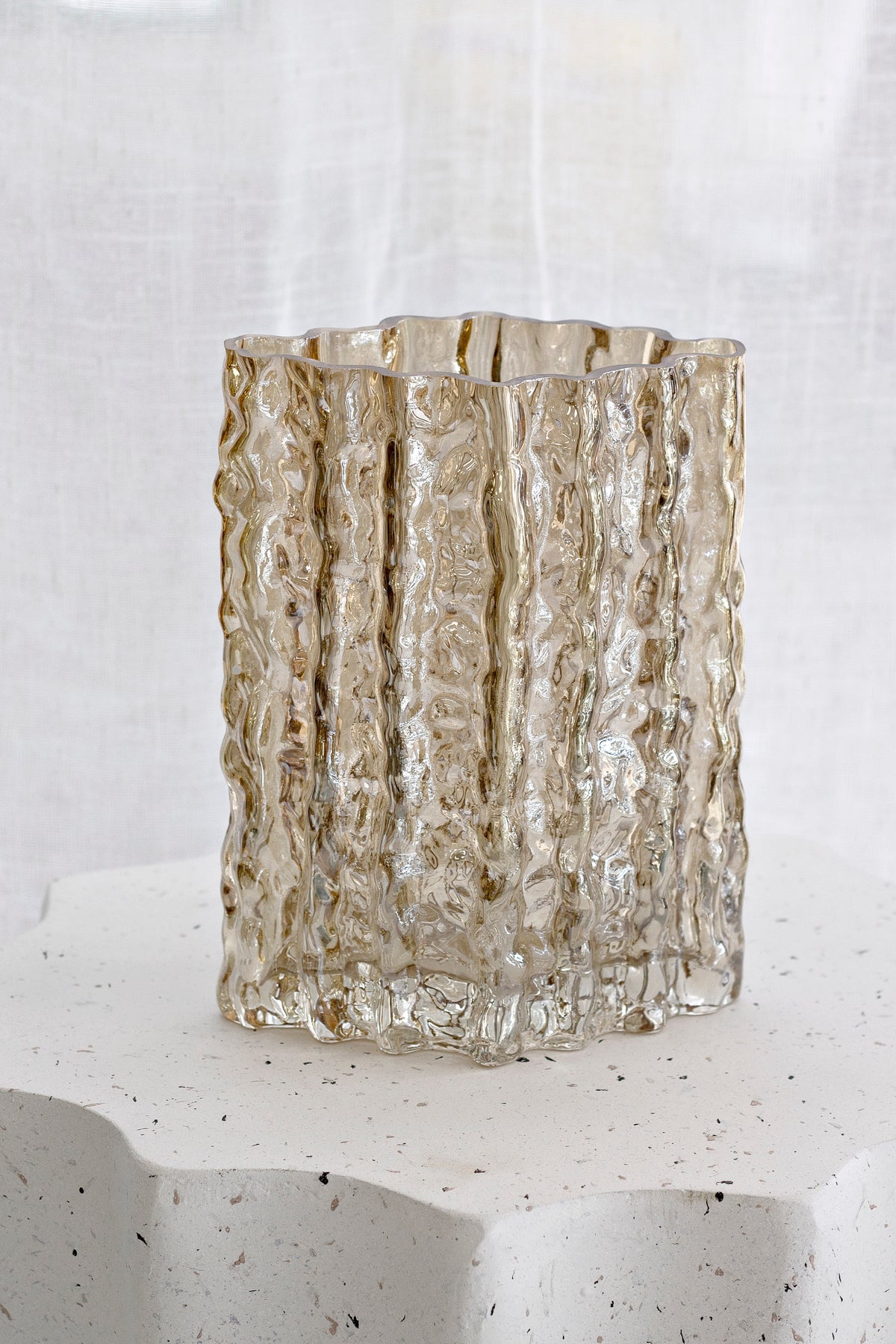 Gold Glacier vase resting on a scalloped stone base in warm afternoon light