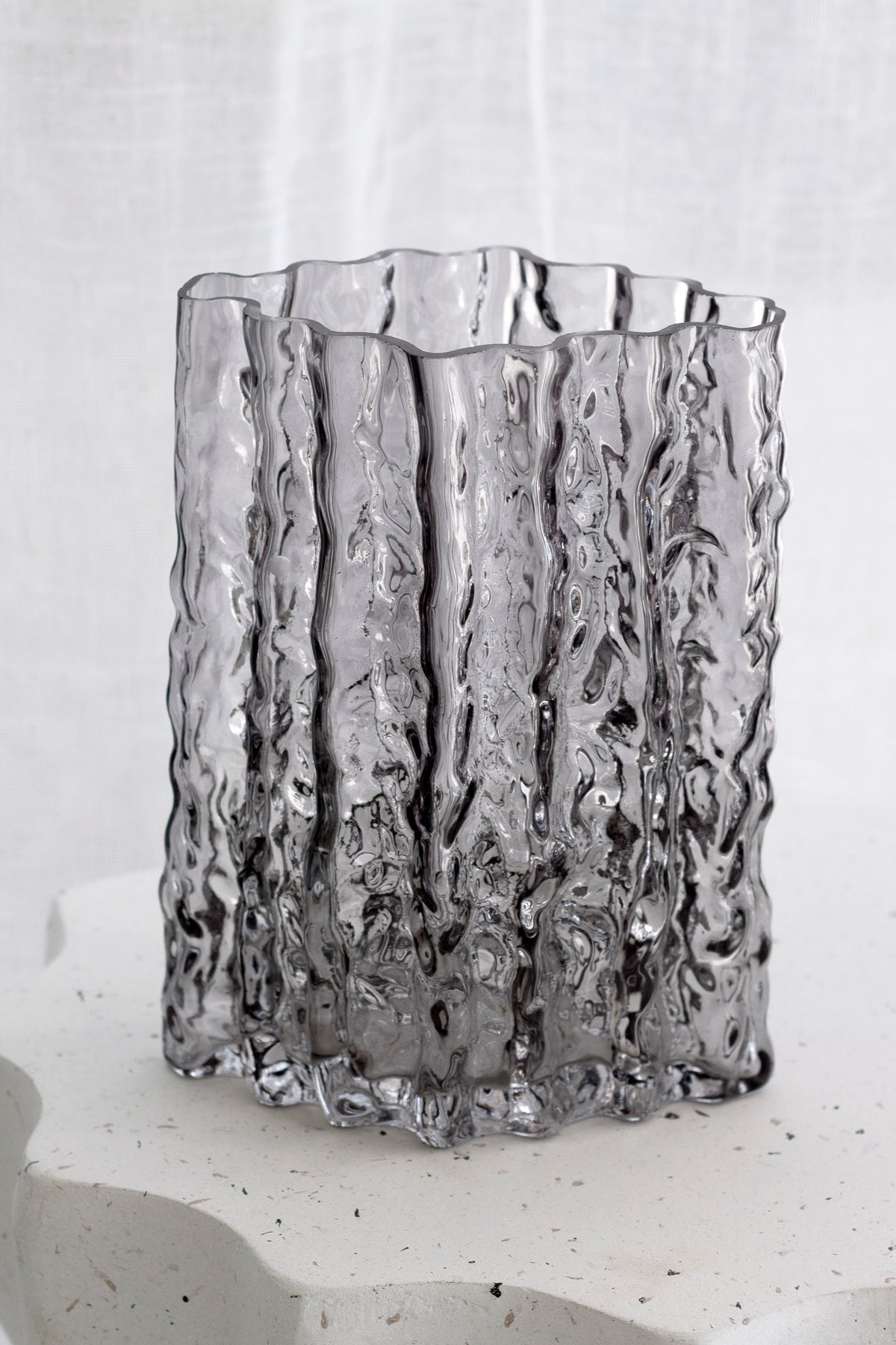 Smoke Glacier vase standing alone on a wavy stone plinth against a grey backdrop