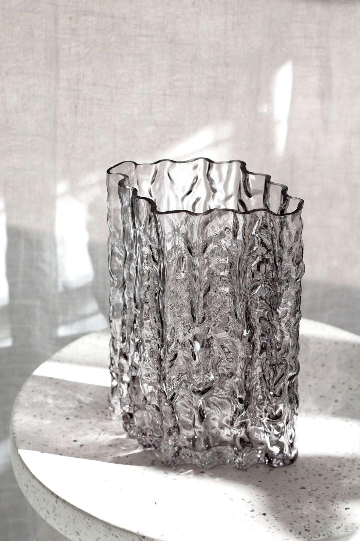 Smoke Glacier vase side on atop a stone pedestal, sunlight and shadow behind