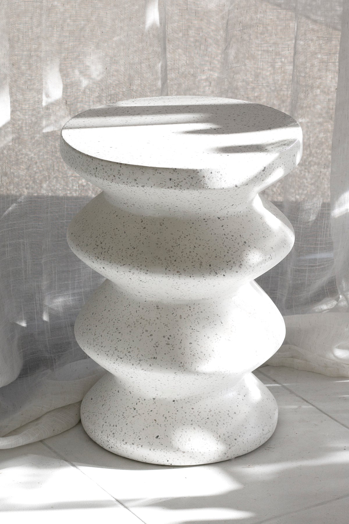 Nara stool in white speckled stone in sunlight against a textured wall