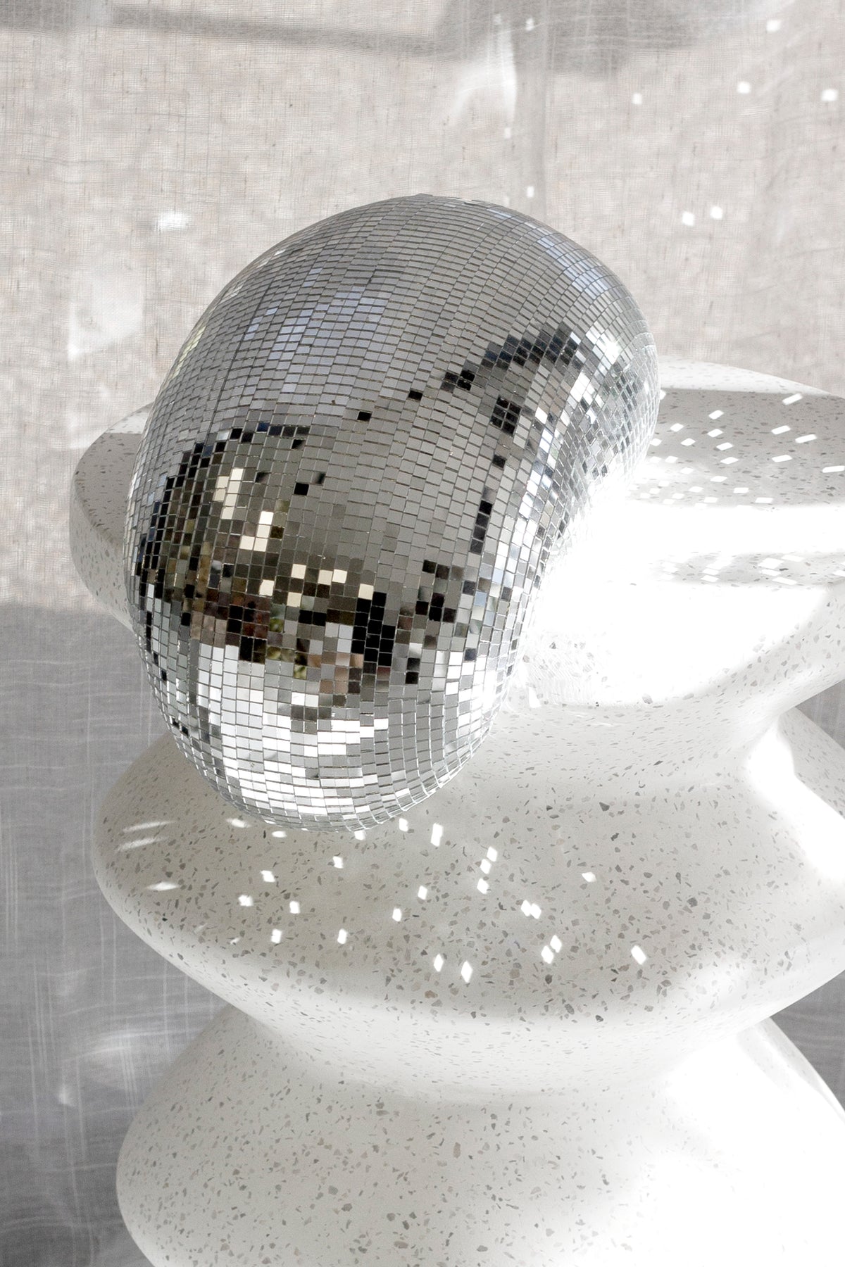 Nara stool in white speckled stone with a mirrored disco ball resting on top