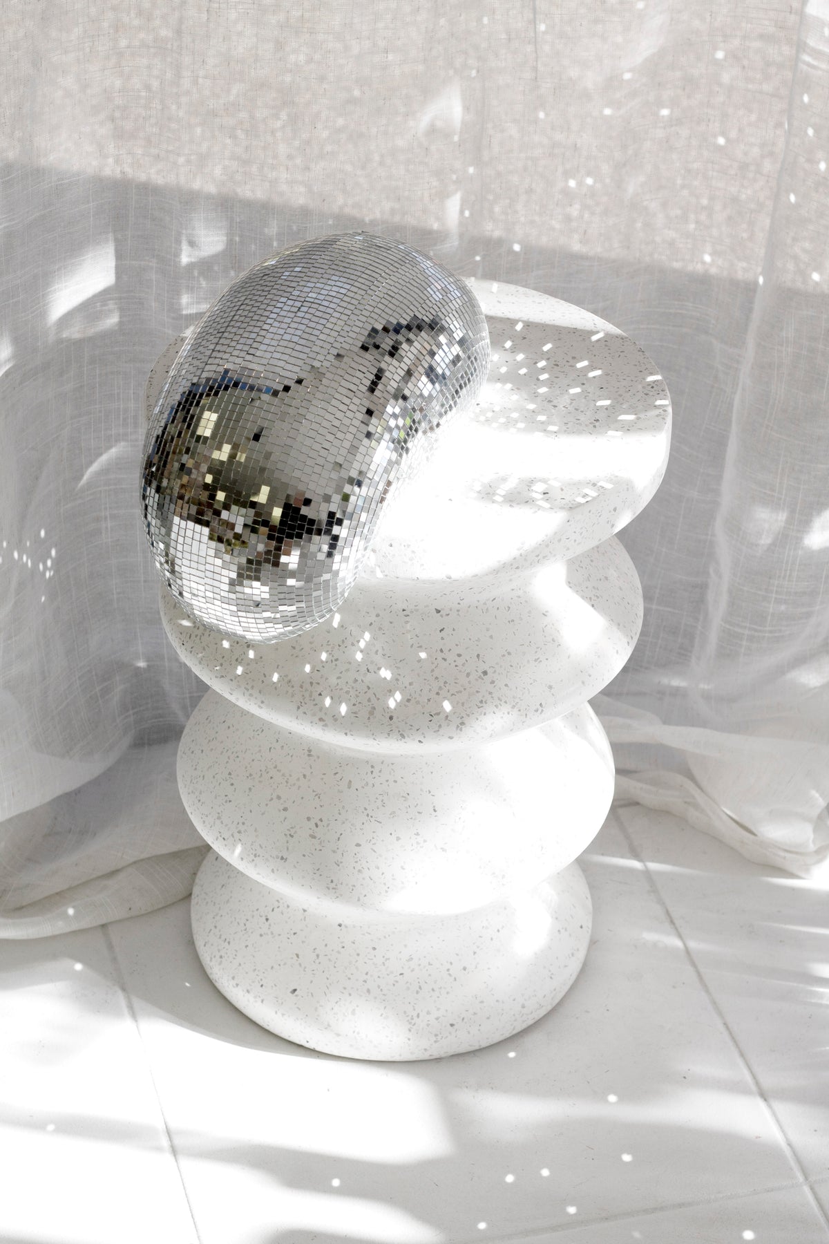 Melting disco ball balanced on a white fluted pedestal in sunlight