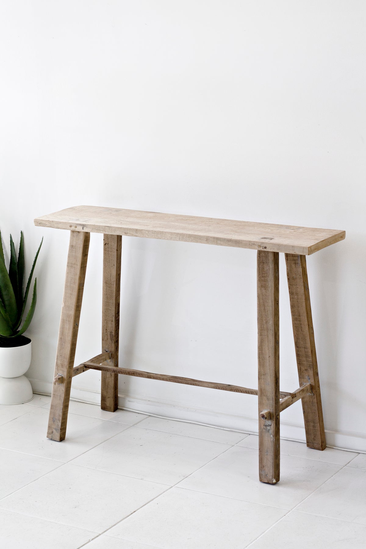 Recycled teak console table in a plain white room beside a snake plant