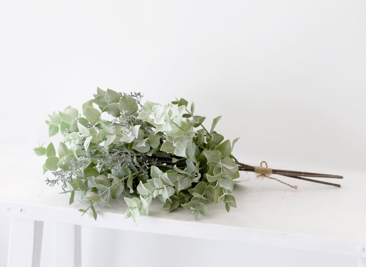 Faux seeded eucalyptus bundle resting on a white table