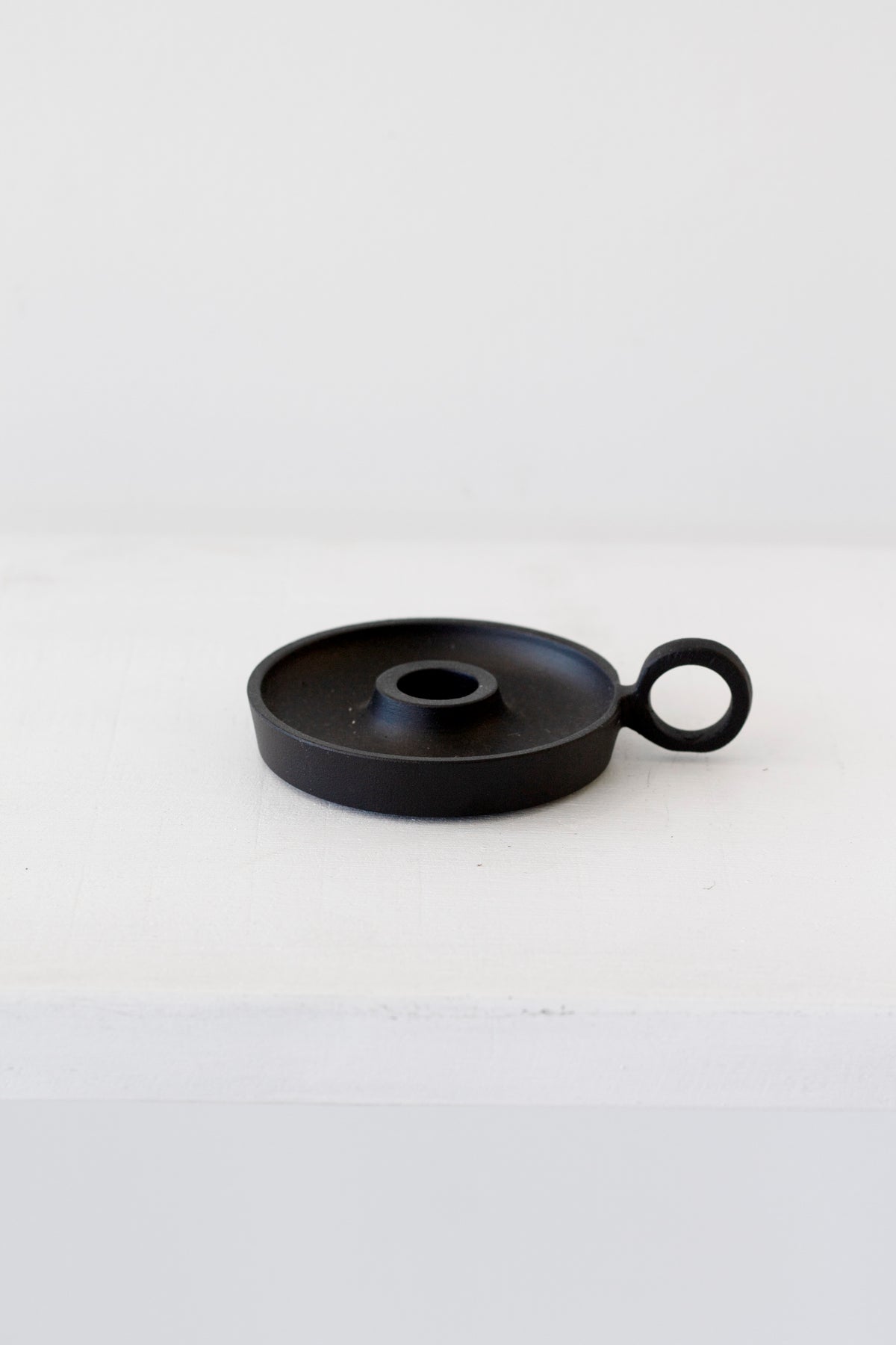 Black taper candle holder with its ring handle, resting on a white painted ledge