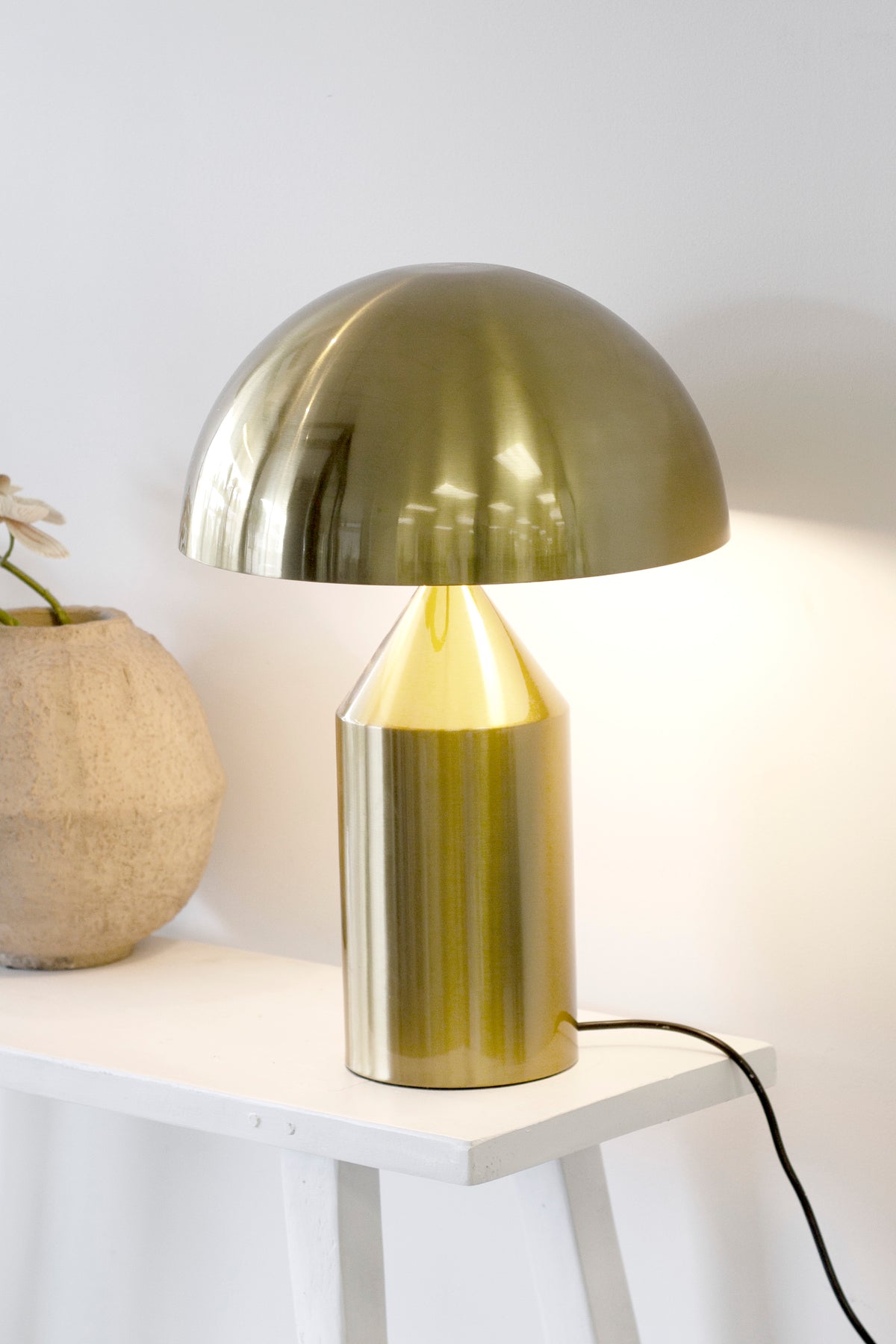 Brass dome lamp lit beside a chalky stone vase holding a single pale bloom