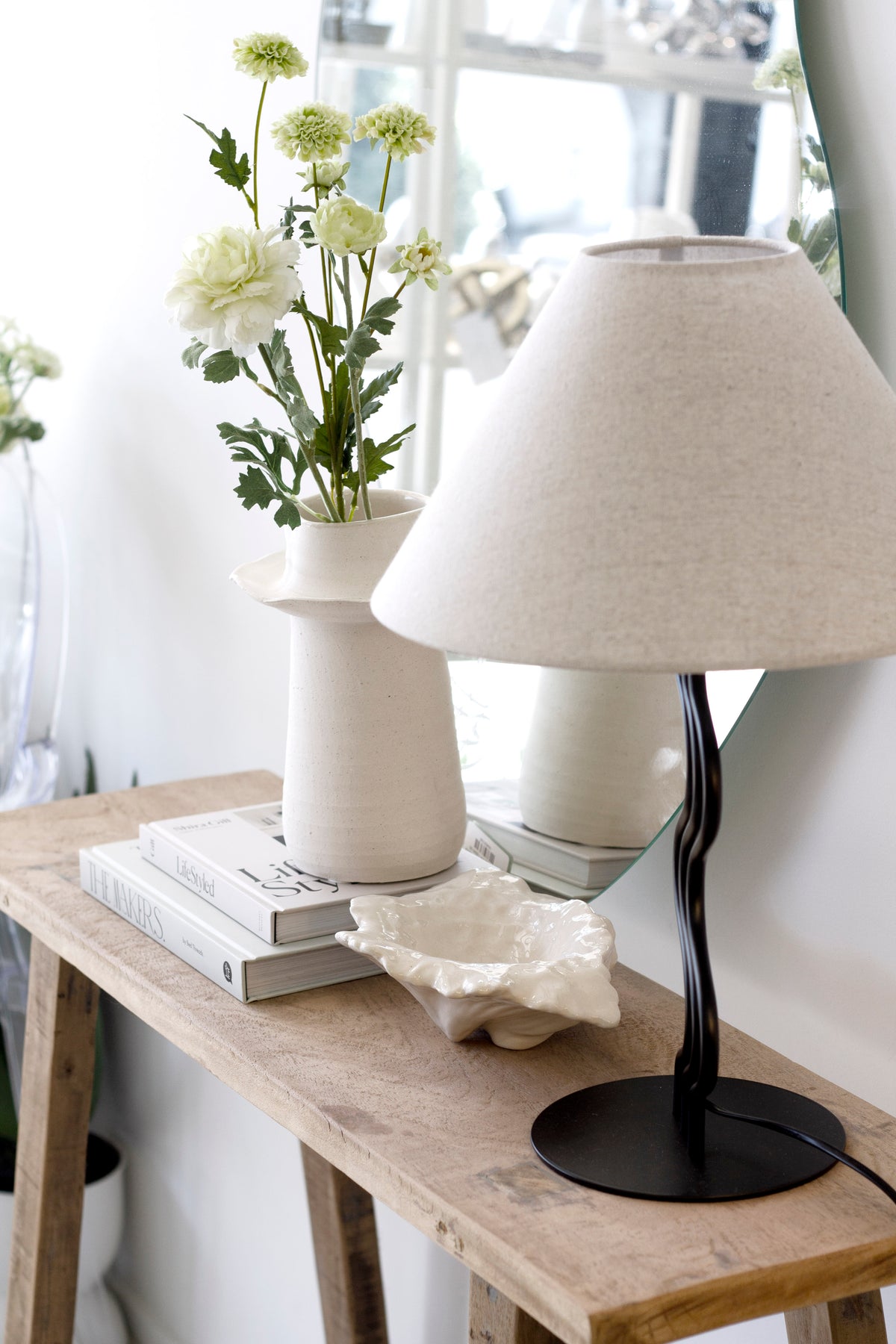 Recycled teak console styled with a cream lamp, white vase of daisies and books by a window